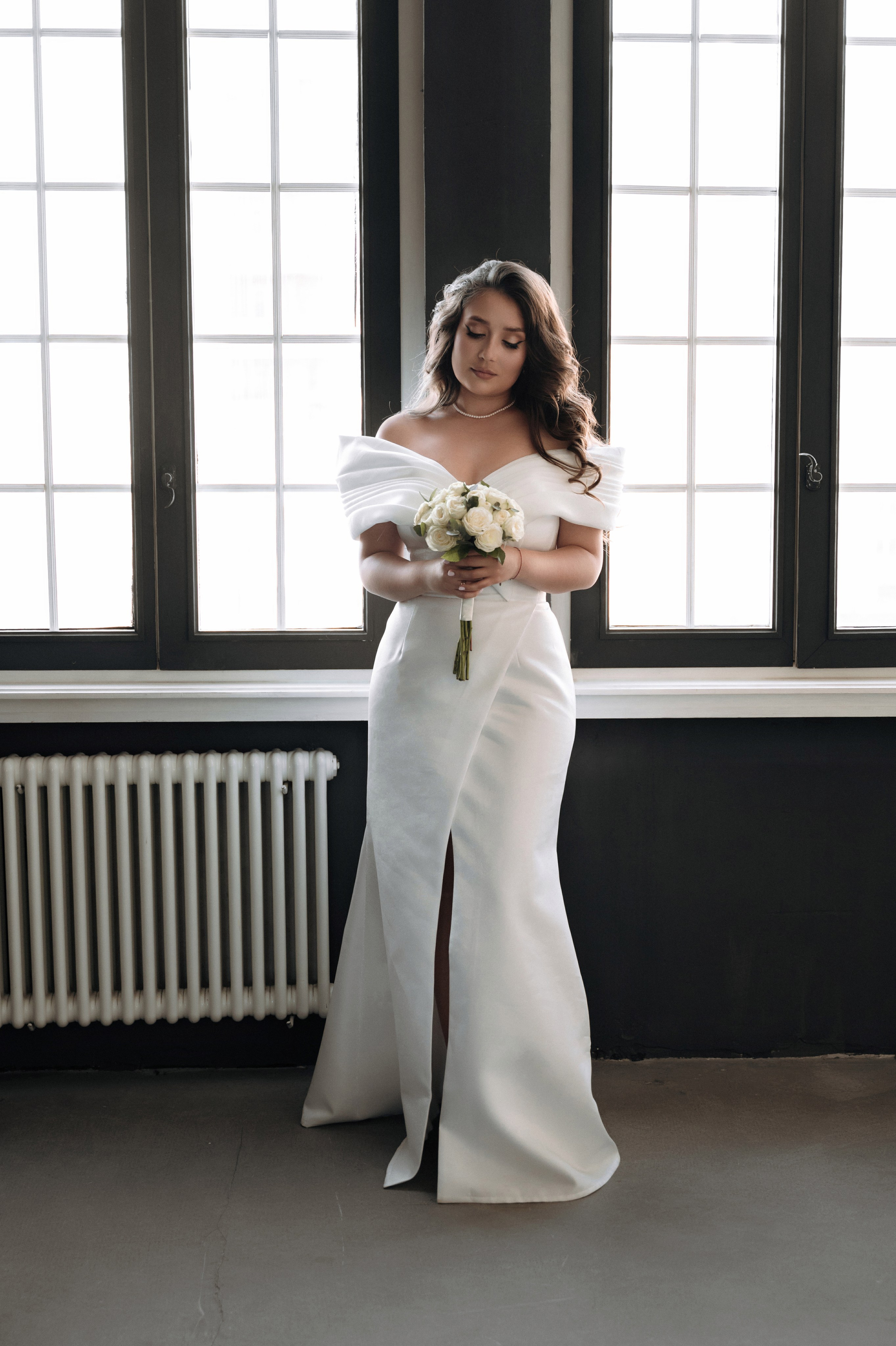 Невеста в белом платье с букетом у окна