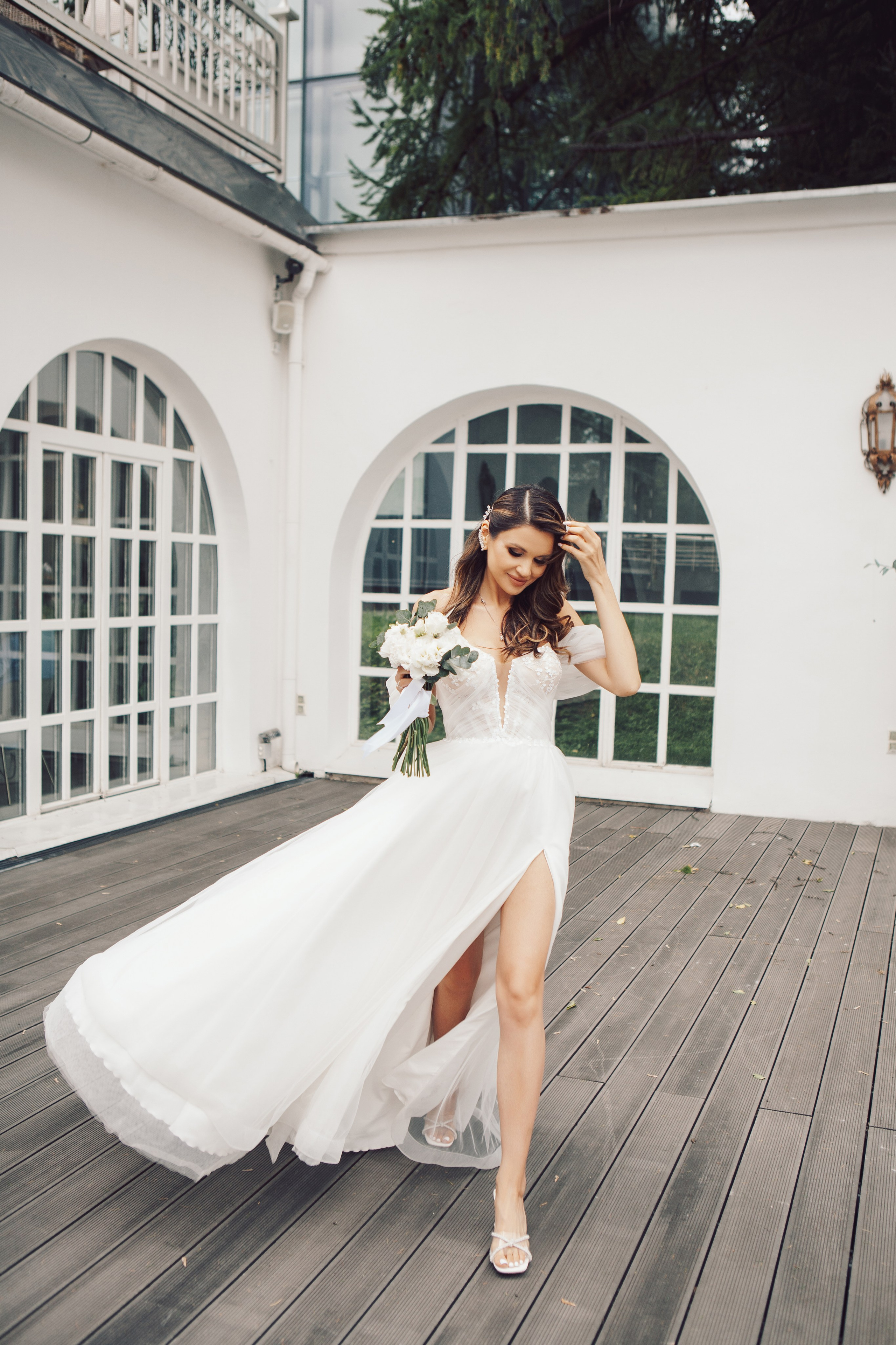 Шикарная невеста в стильном платье и с букетом идет у ресторана