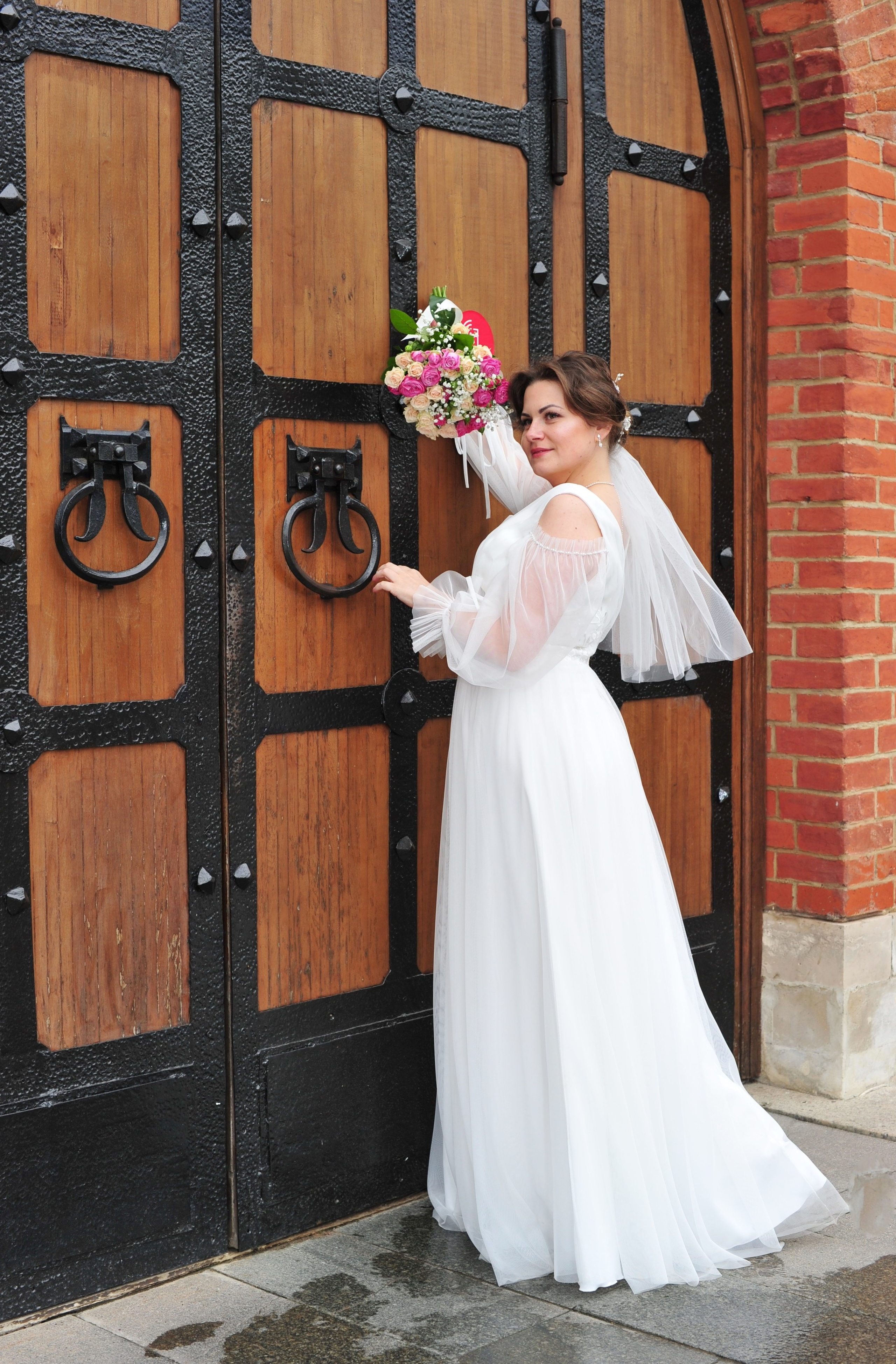 Свадьба в Царицыно пасмурным летним днем, невеста стоит на фоне старинной кованой деревянной  двери