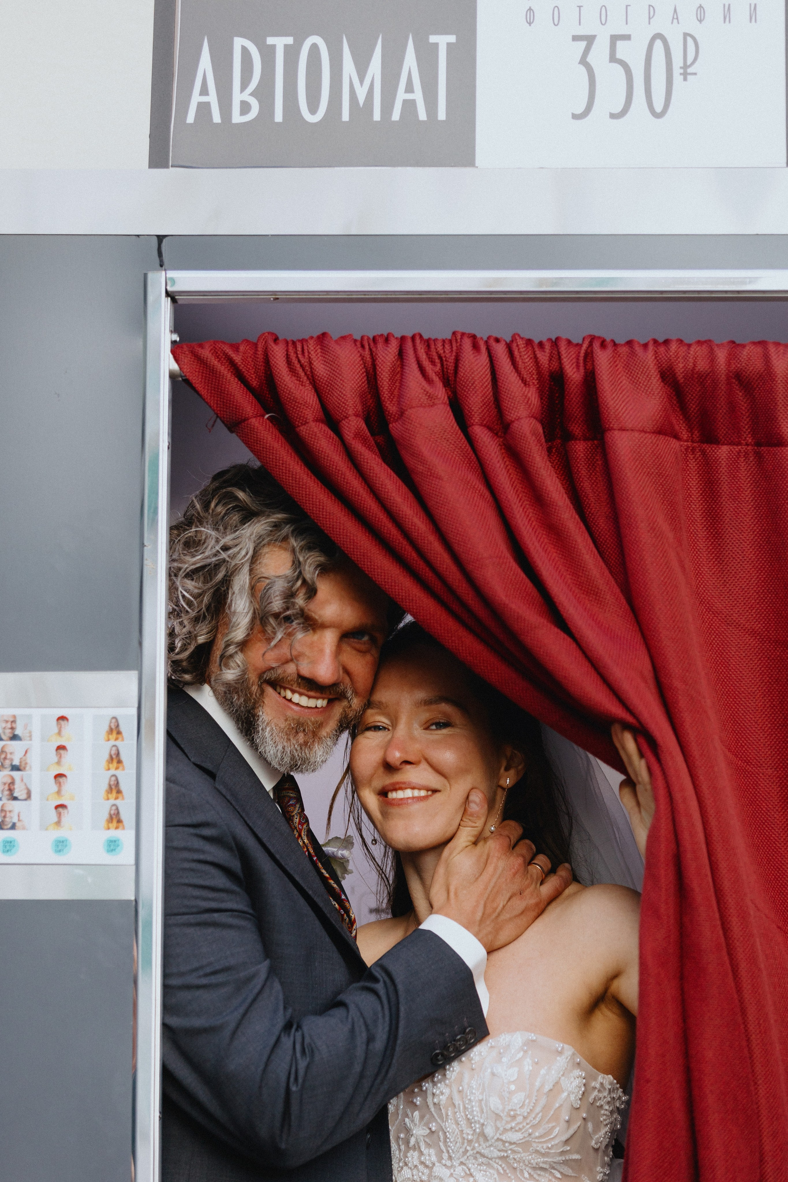 Яркие свадебные фото в фотобудке: жених и невеста счастливо улыбаются из-за красных штор. Оригинальные идеи для свадебной фотосессии.