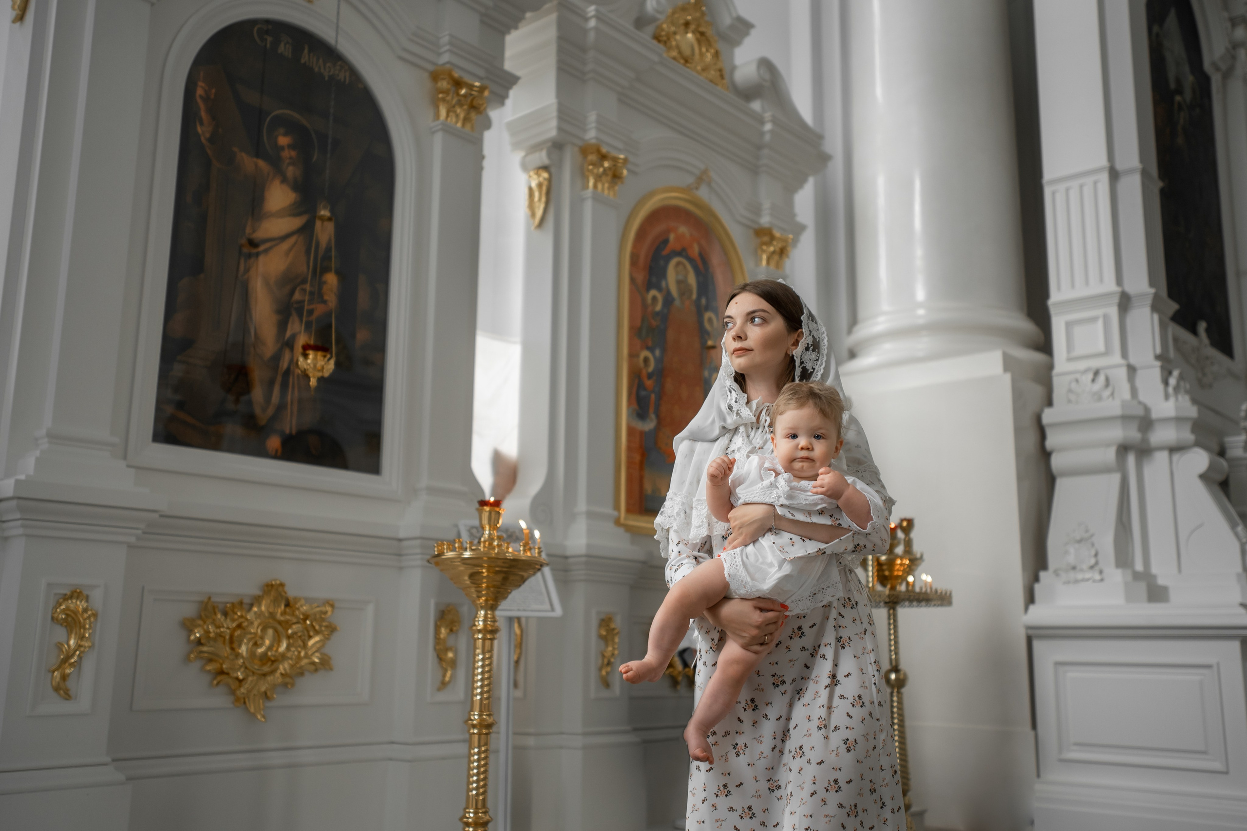мама с младенцем на руках смотрит вдаль на фоне пышных интерьеров Смольного собора