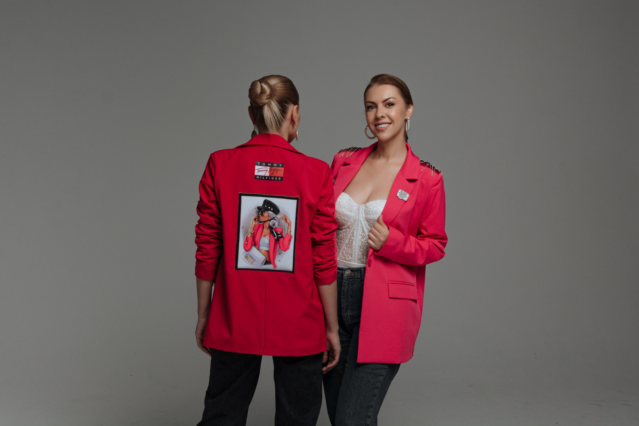  Яркие краски весны: две подруги позируют в ярких красных пиджаках на фоне студийных цветов и зелени, излучая теплоту и радость.