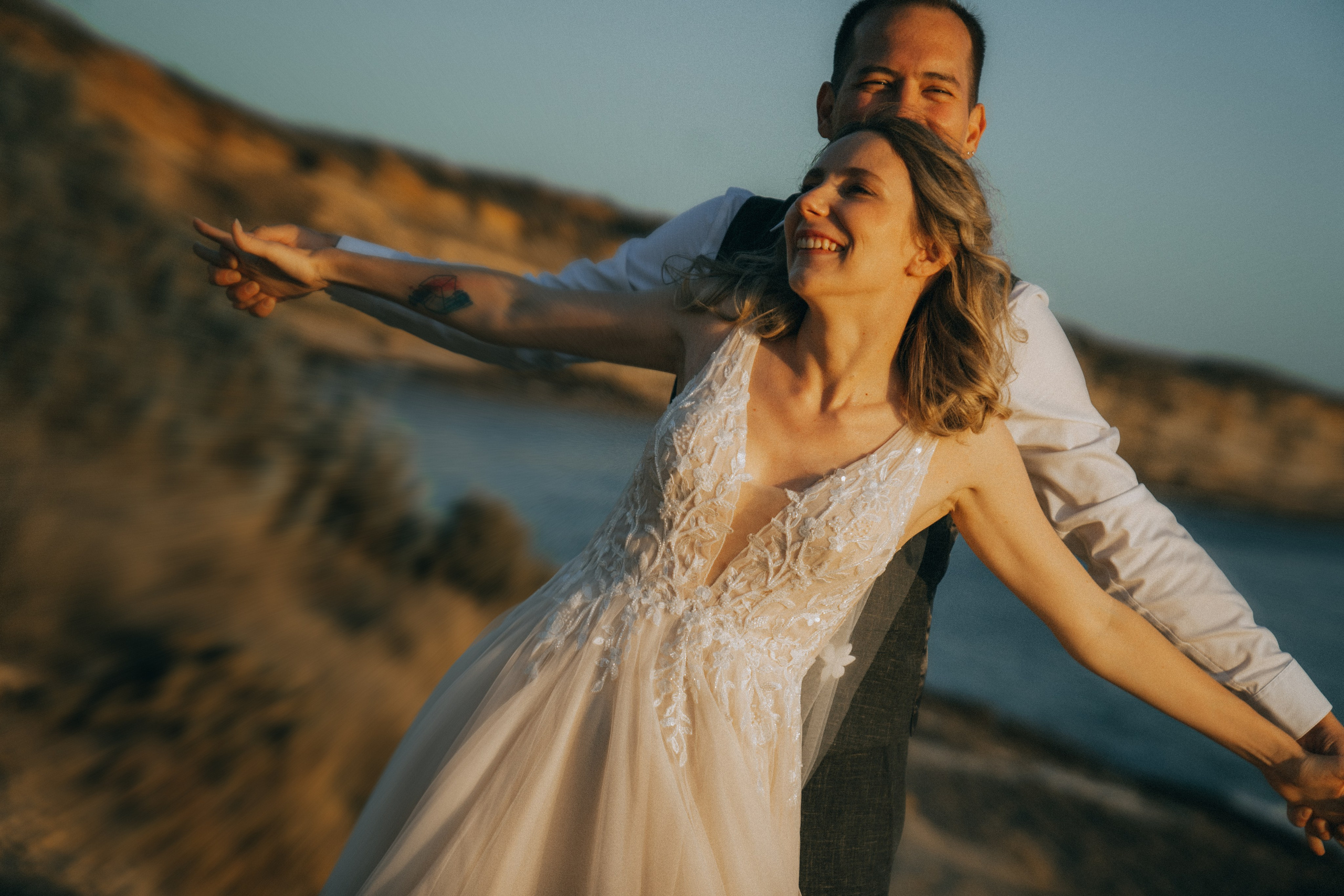 Счастливая пара жених и невеста целуется на фоне волн  скал и заката у океана.