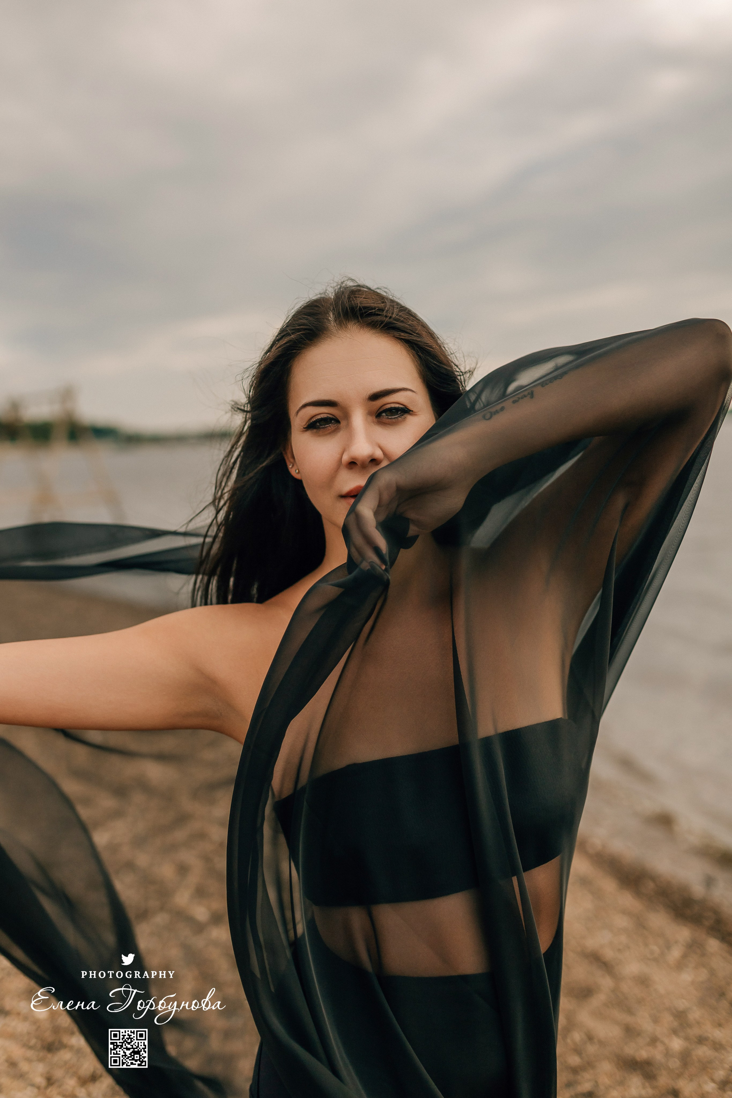 Фотосессия с черной тканью. Легкая черная вуаль летит на вертру. Фотосессия у реки черная серия с тканью. Девушка укуталась в черную ткань. Прогулка по набережной. Песок, речка, модель в черном. Качели над водой, Закат. Девушка лежит на песке. В зеленых деревьях