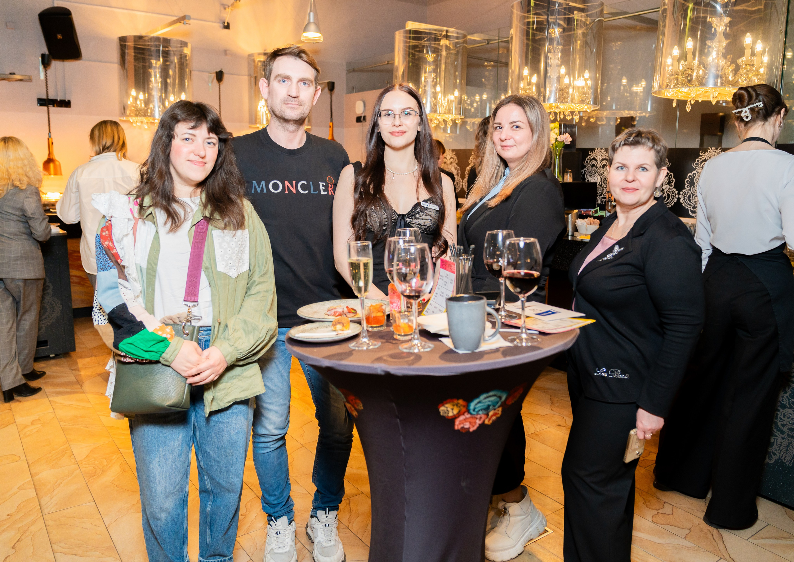 Гости мероприятия позируют у стола в Radisson Sonya. Мужчина в чёрной футболке Moncler и женщины в стильных образах. Автор фото Евгений Мальцев.