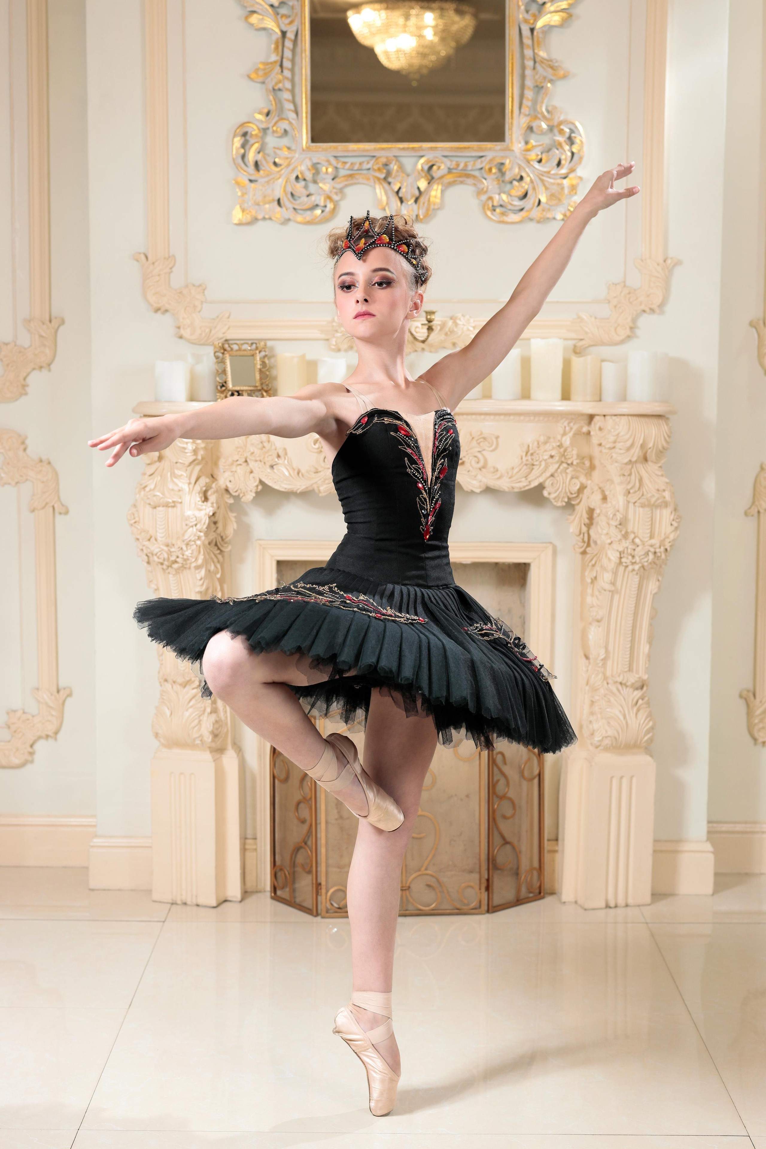 Девочка в чёрном балетном платье в полный рост на фоне камина.