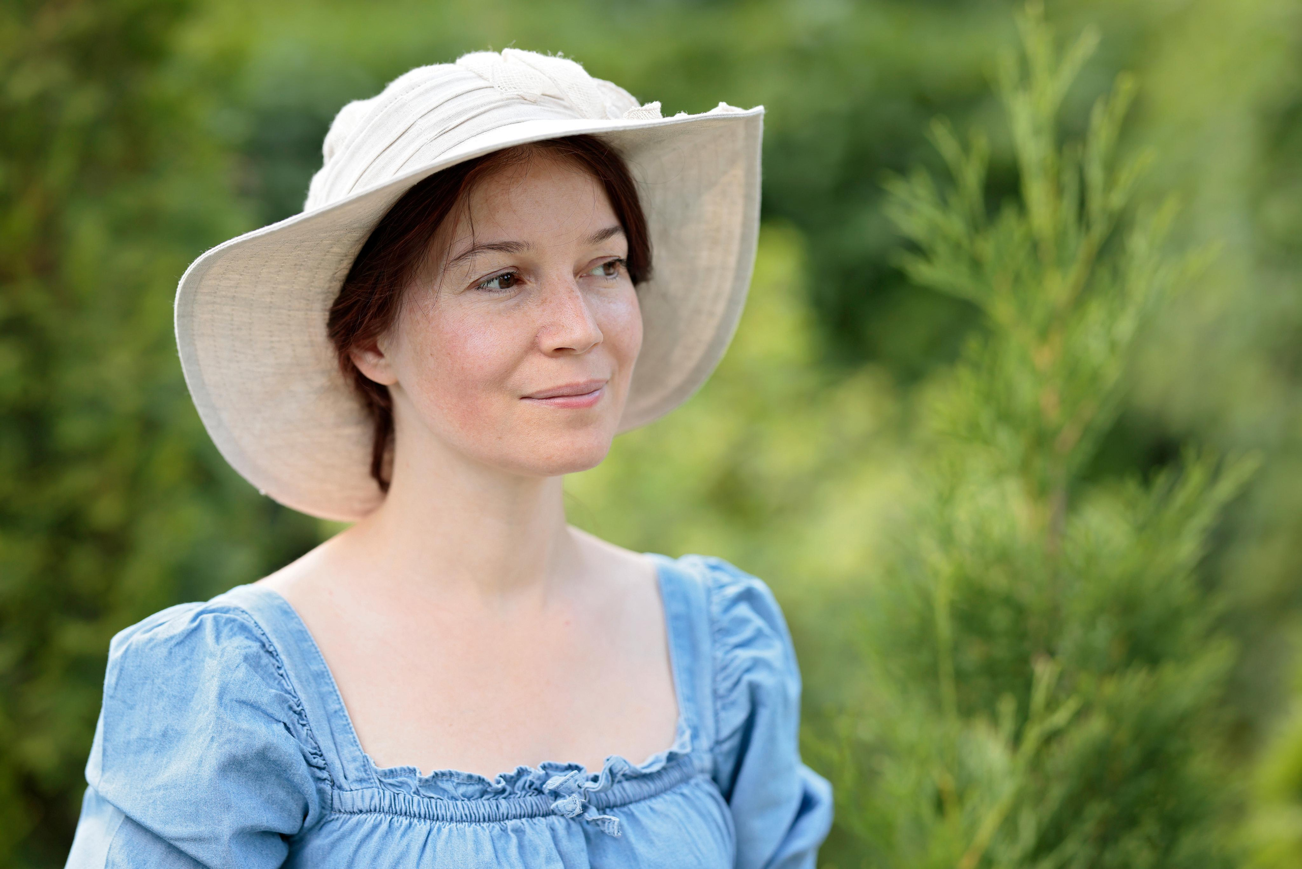 Портрет женщины в шляпе и голубом платье на фоне зелени.