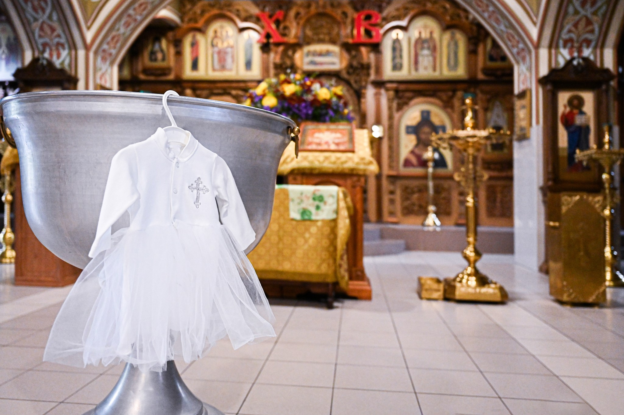 Фото белой крестильной рубашки младенца на фоне купели и икон