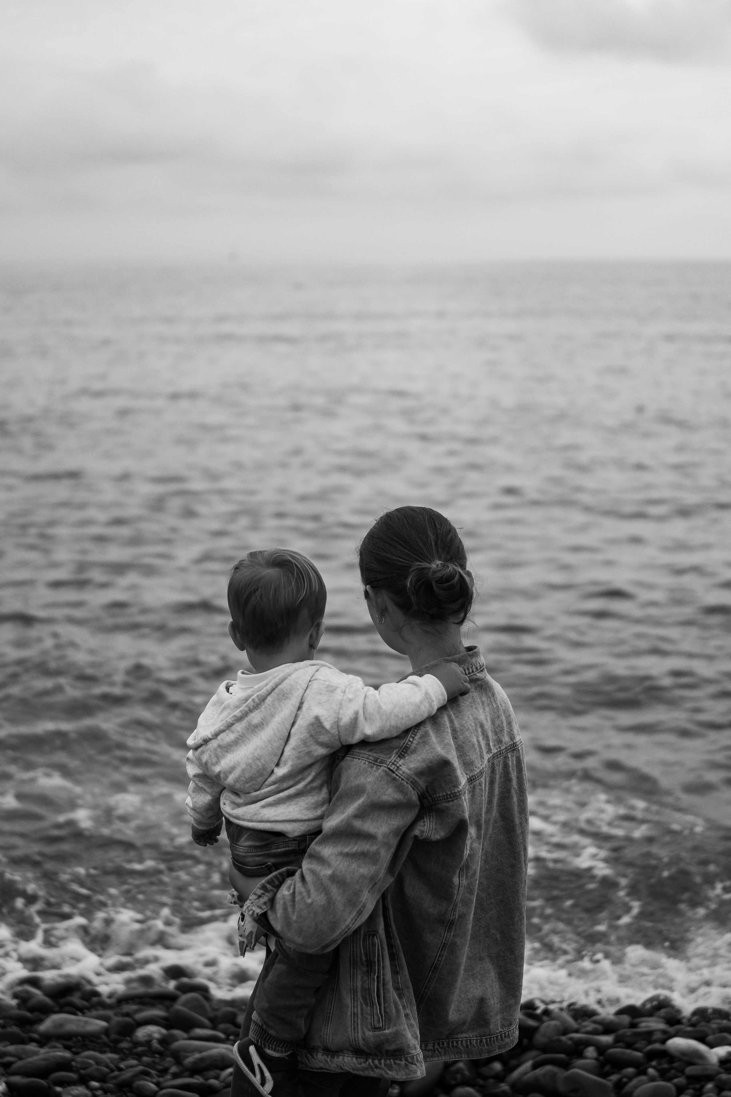 мама держит на руках ребенка глядя на море 