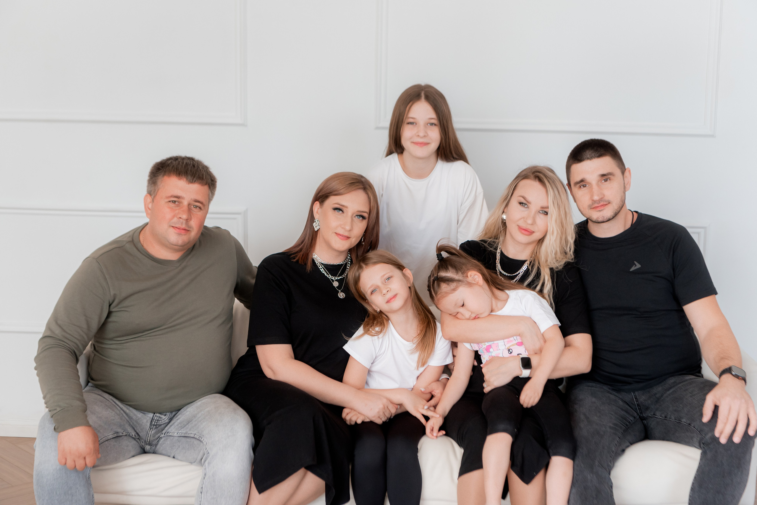 Две больших семьи фотографируются в студии на диване и обнимаются