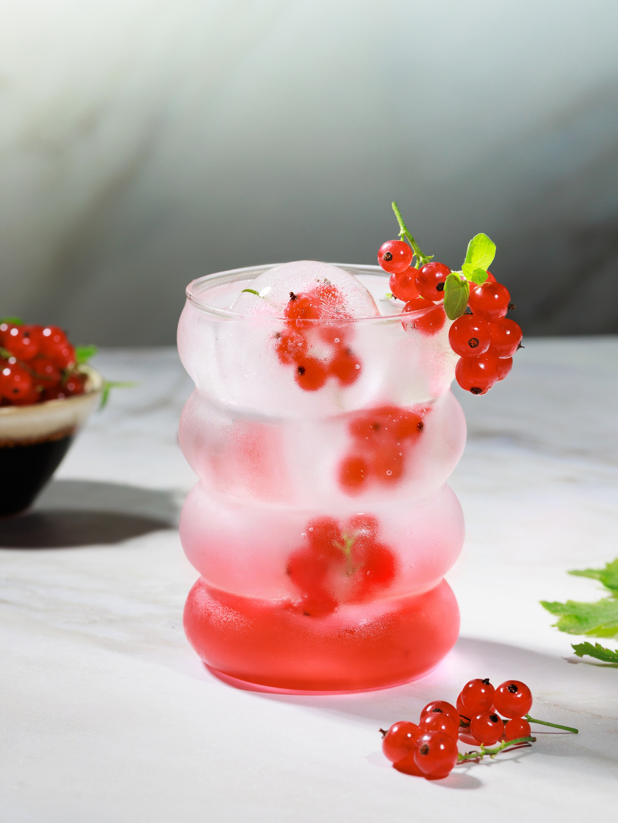 Коктейль с замороженными ягодами красной смородины внутри льда. Фудфото коктейлей
