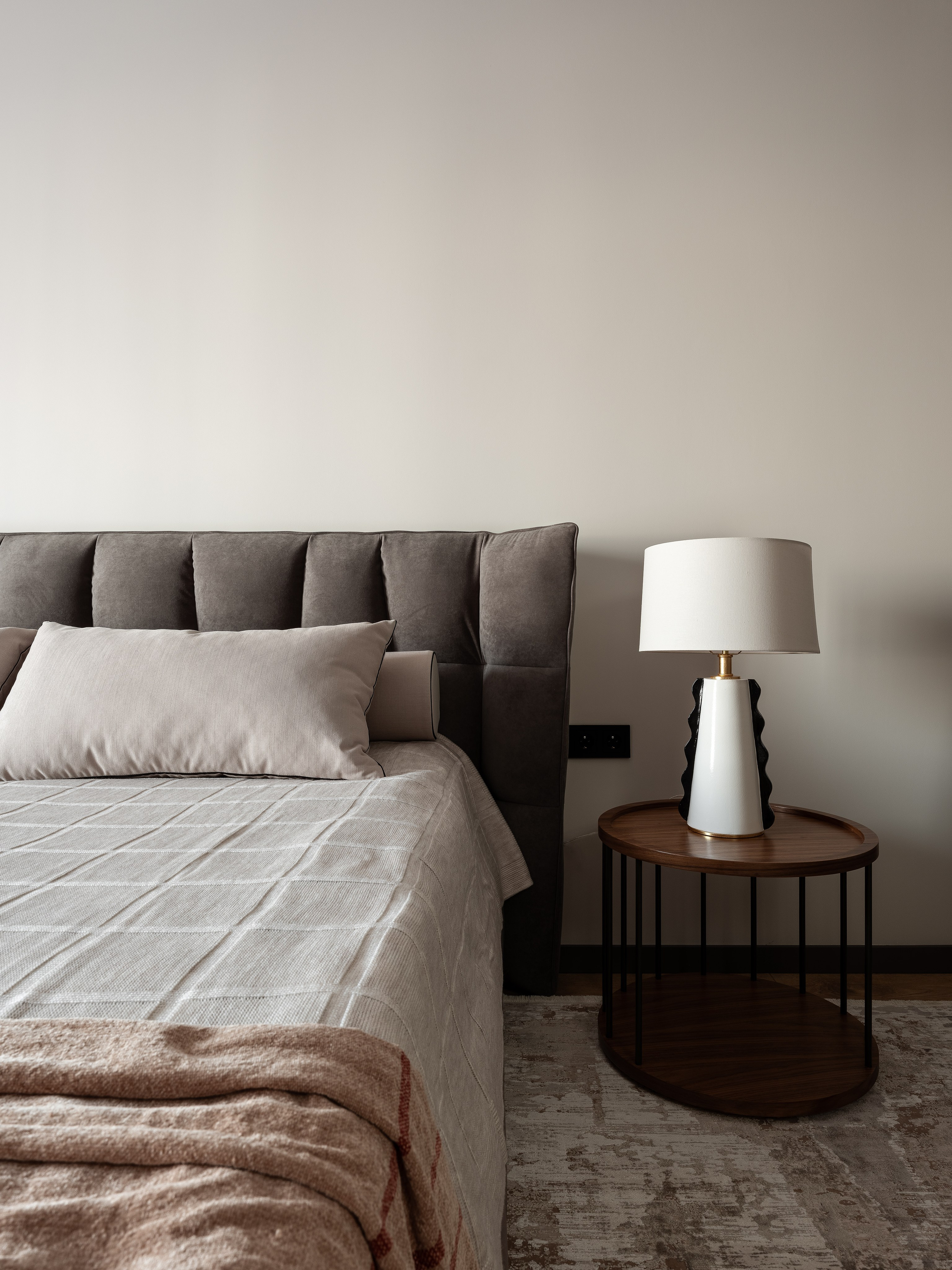 Современная спальня с серым мягким изголовьем, прикроватным столиком из дерева и лампой в минималистичном стиле, дизайнер Екатерина Мищенко, фотограф Сергей Денисенко, гармоничный интерьер в спокойной бежево-серой цветовой гамме.