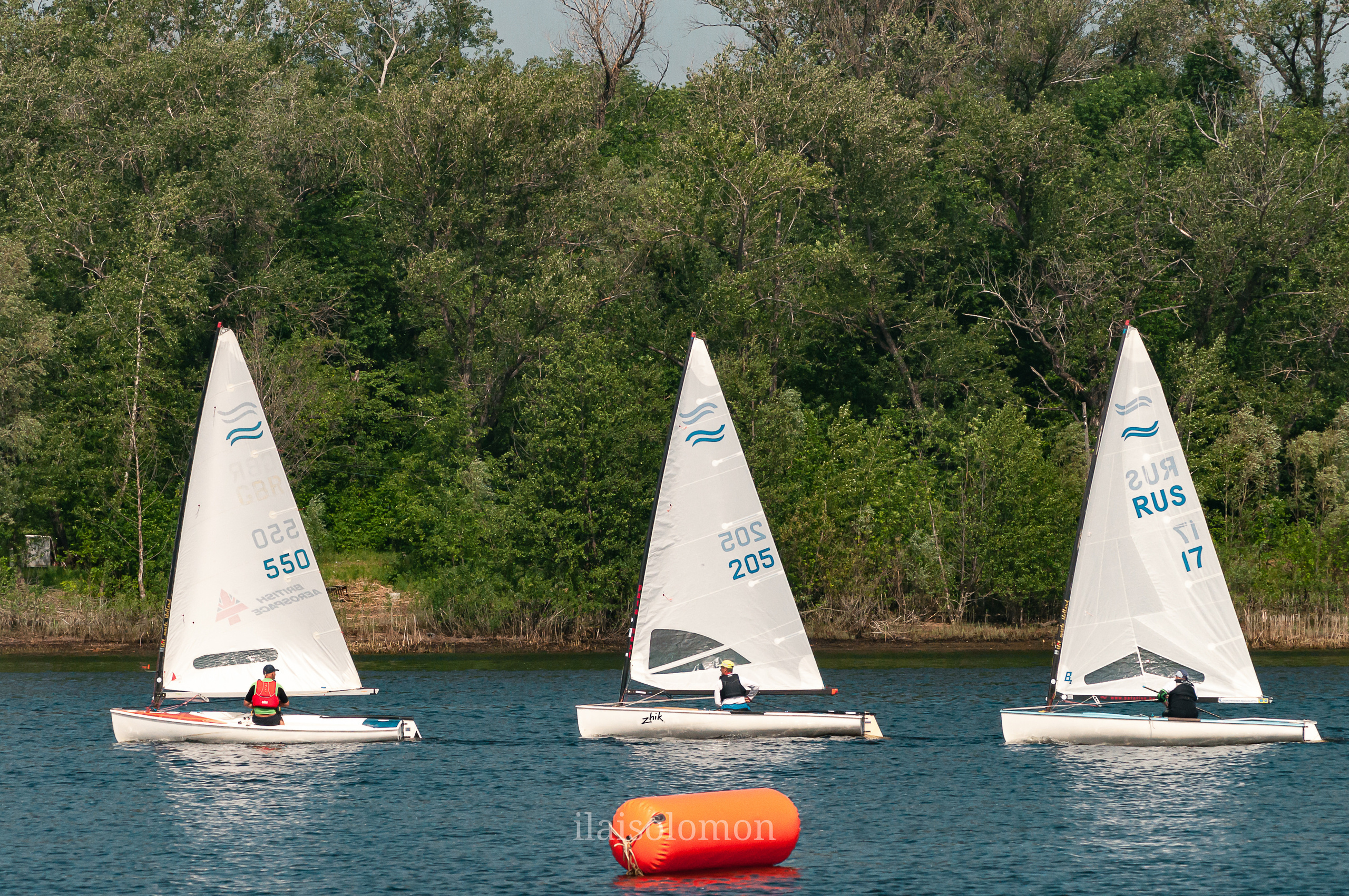 Старт парусной регаты на реке Волге, яхты выстраиваются у зеленого берега. Съёмка спортивного мероприятия.