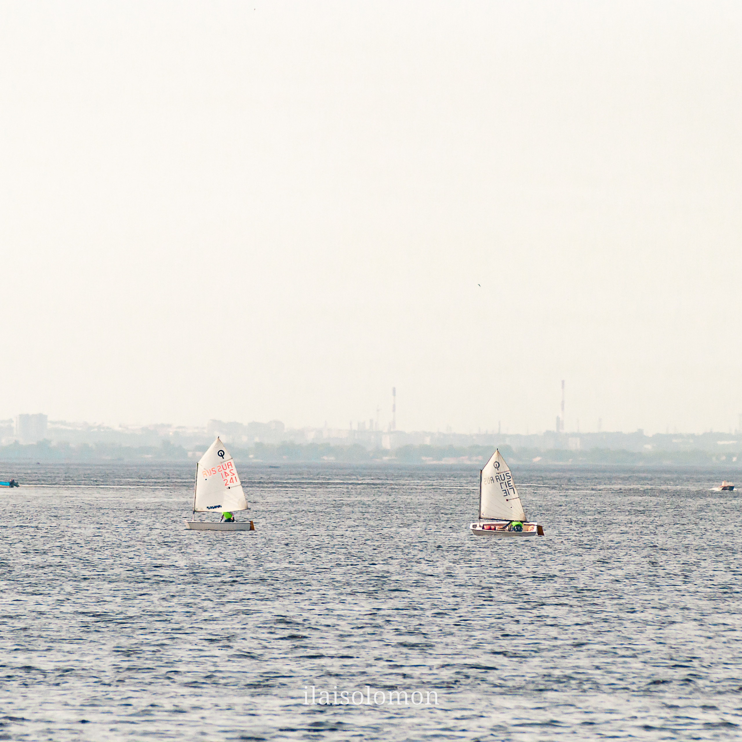 Дети учатся управлять маленькими яхтами на реке вдали от парусной регаты.