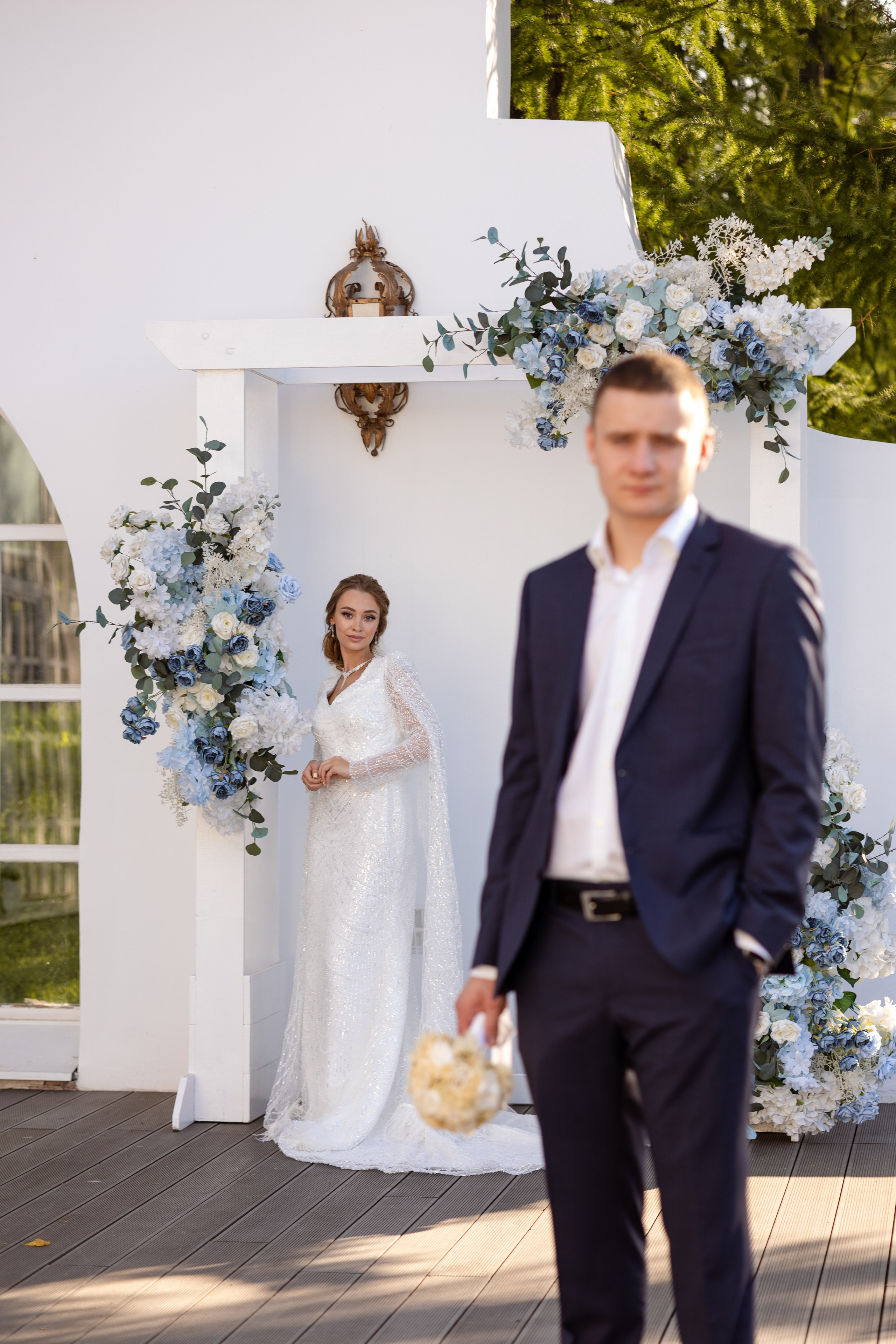 Молодые на фоне белой стены, жених на переднем плане.