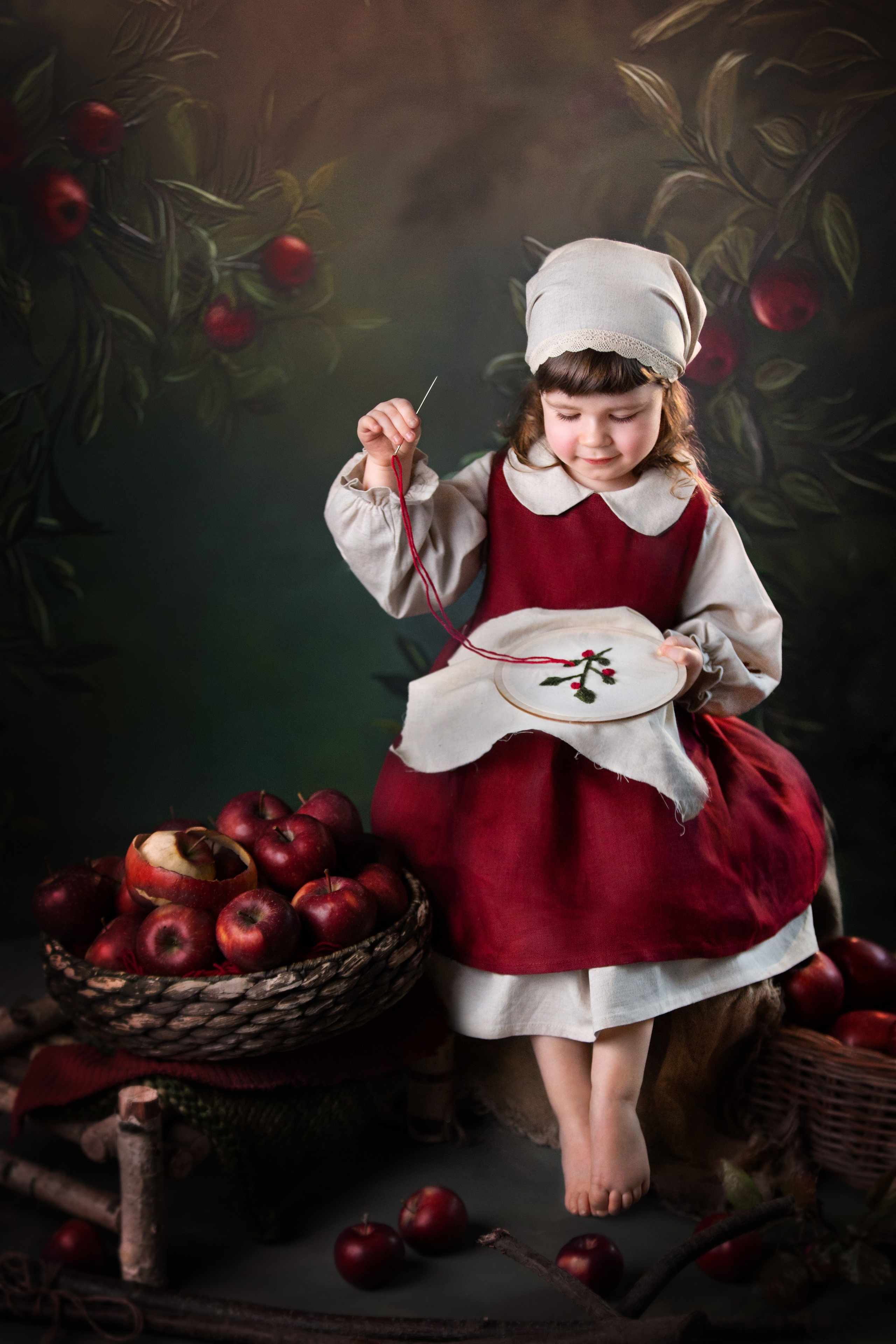 Маленькая девочка вышивает иглой, рядом с ней стоят яблоки в бадейке. Девочка одета в старинную льняную одежду, косынку и фартук.