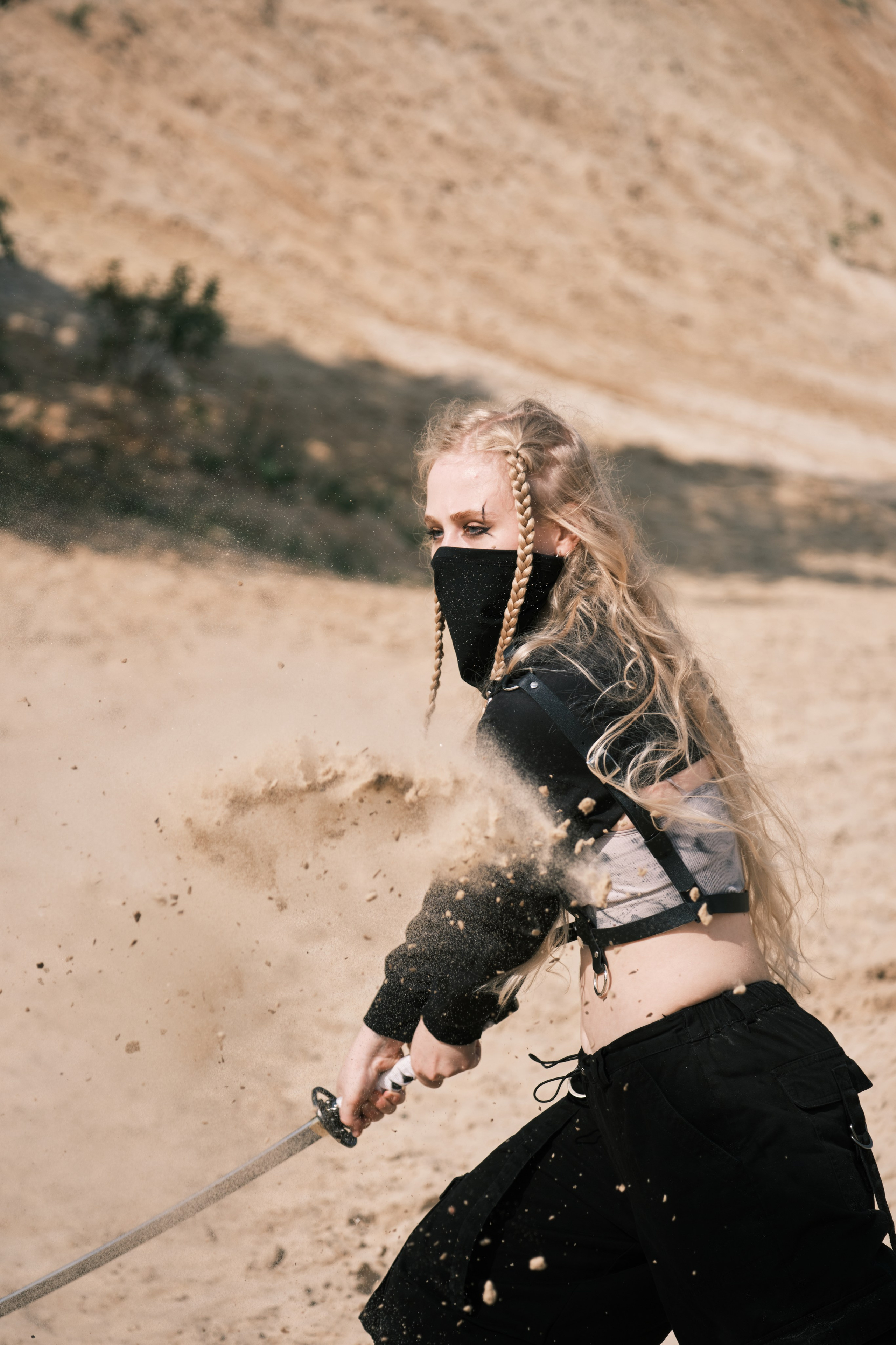 Светловолосая девушка с катаной в руке и черной маске на лице стоит в боевой стойке