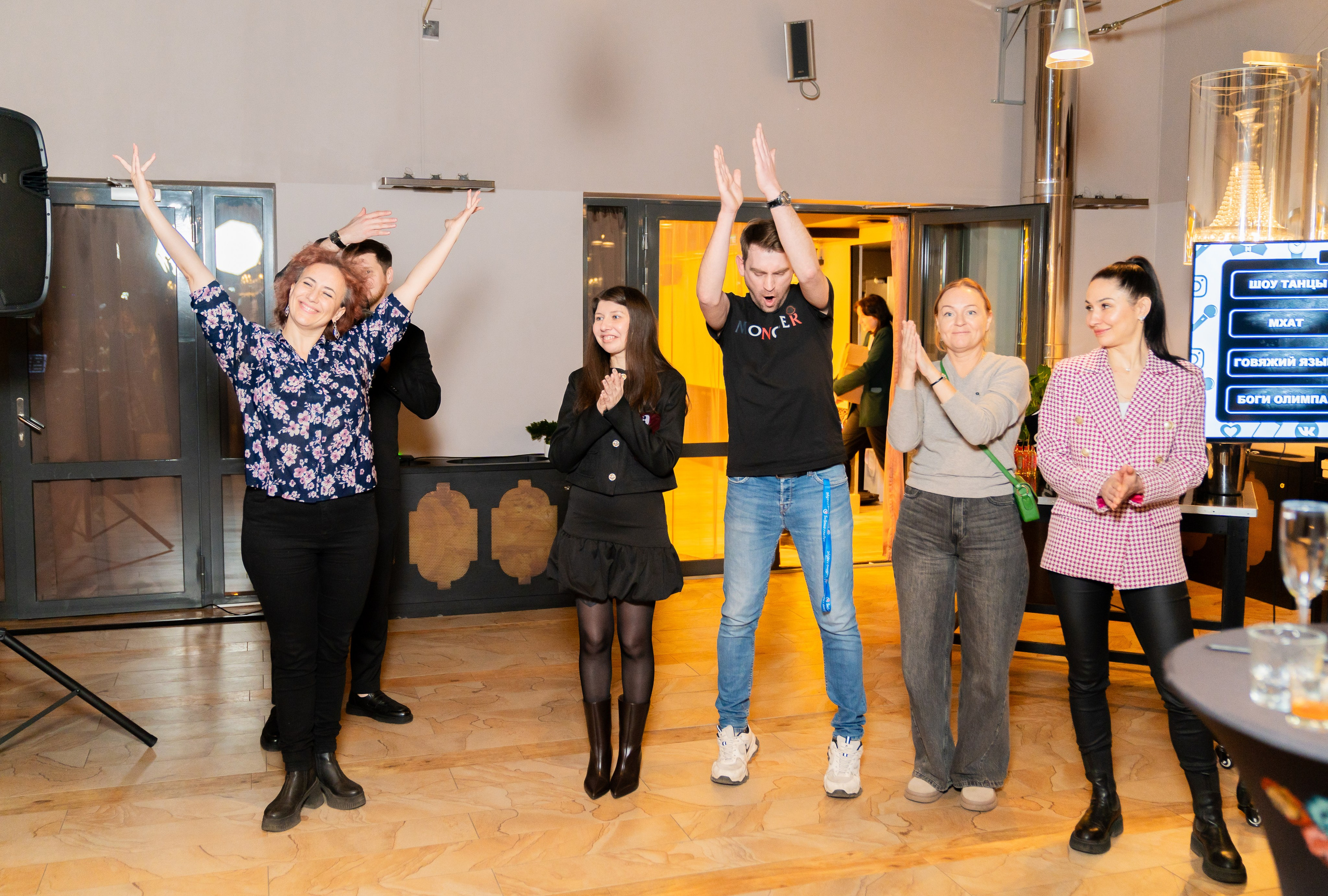 Участники мероприятия в Radisson Sonya радостно аплодируют и поднимают руки. Женщина в розовом жакете и мужчина в чёрной футболке Moncler. Фото Евгения Мальцева.