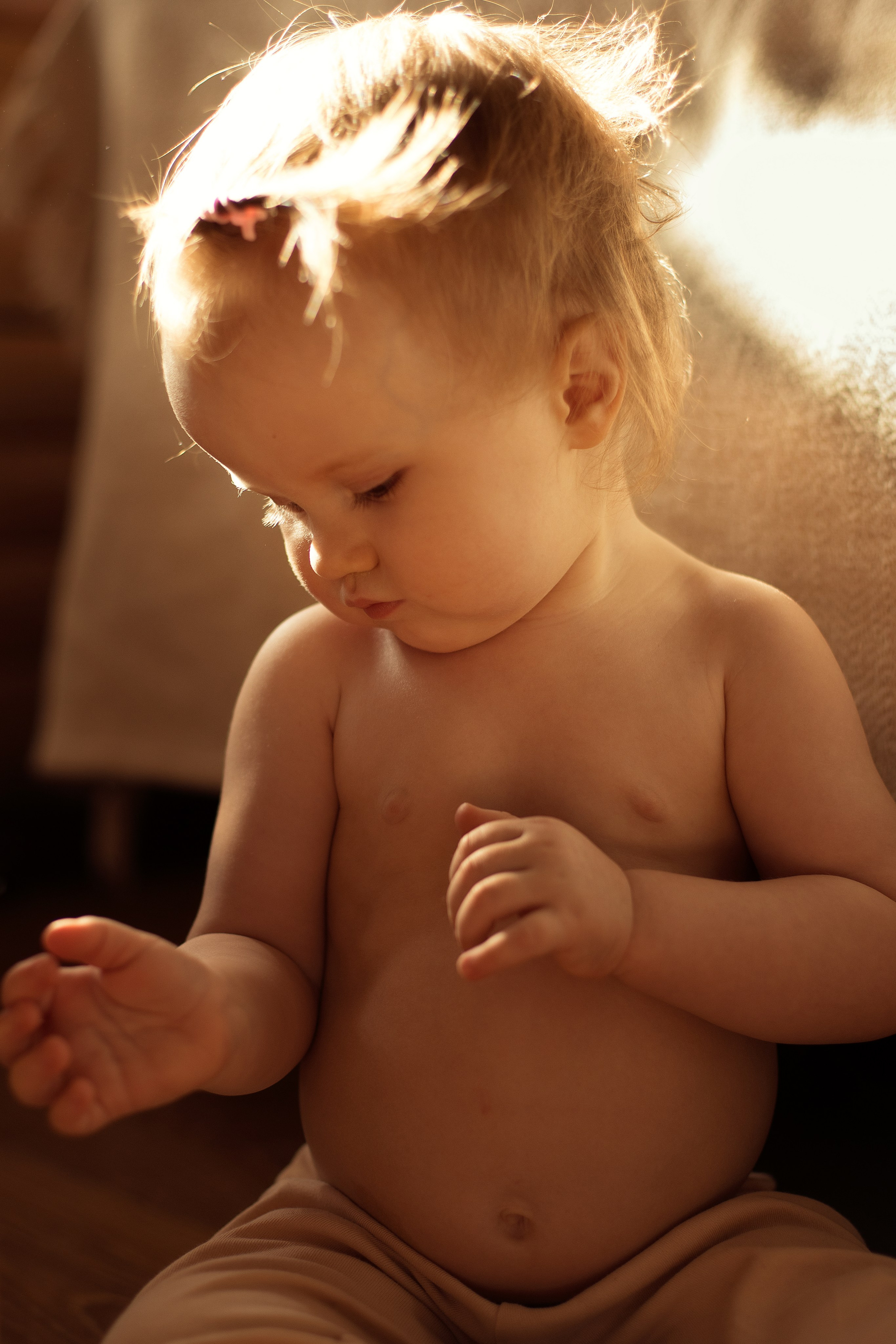 Девочка с голым животиком сидит и рассматривает свои ручки в лучах солнечного света