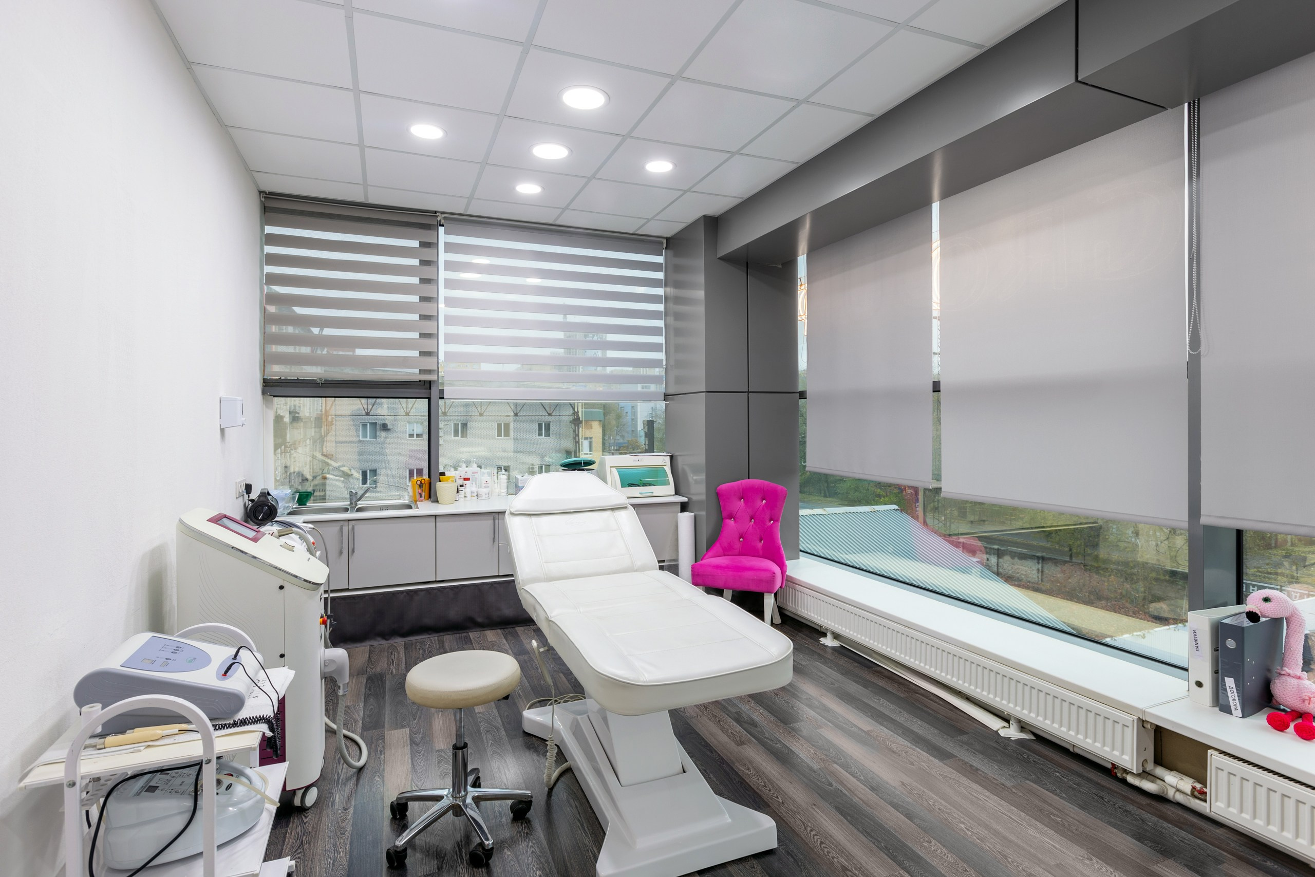 Косметологический кабинет вид внутри. Кабинет в центре косметологии. Кресло косметолога кожаное белое молочное. Кабинет с большими окнами и жалюзи.