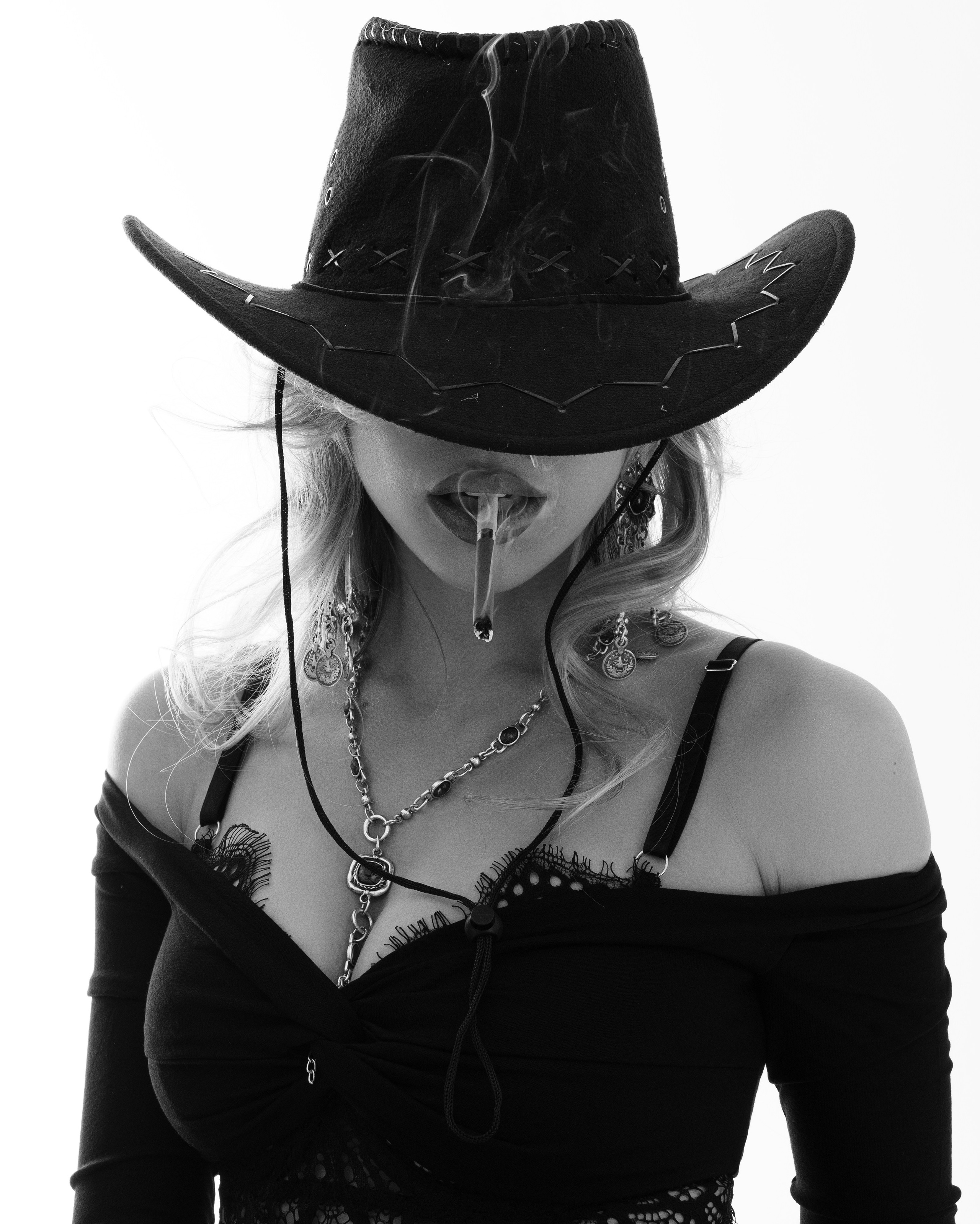 Женщина в ковбойской шляпе с сигарой во рту, в чёрной одежде с открытыми плечами.