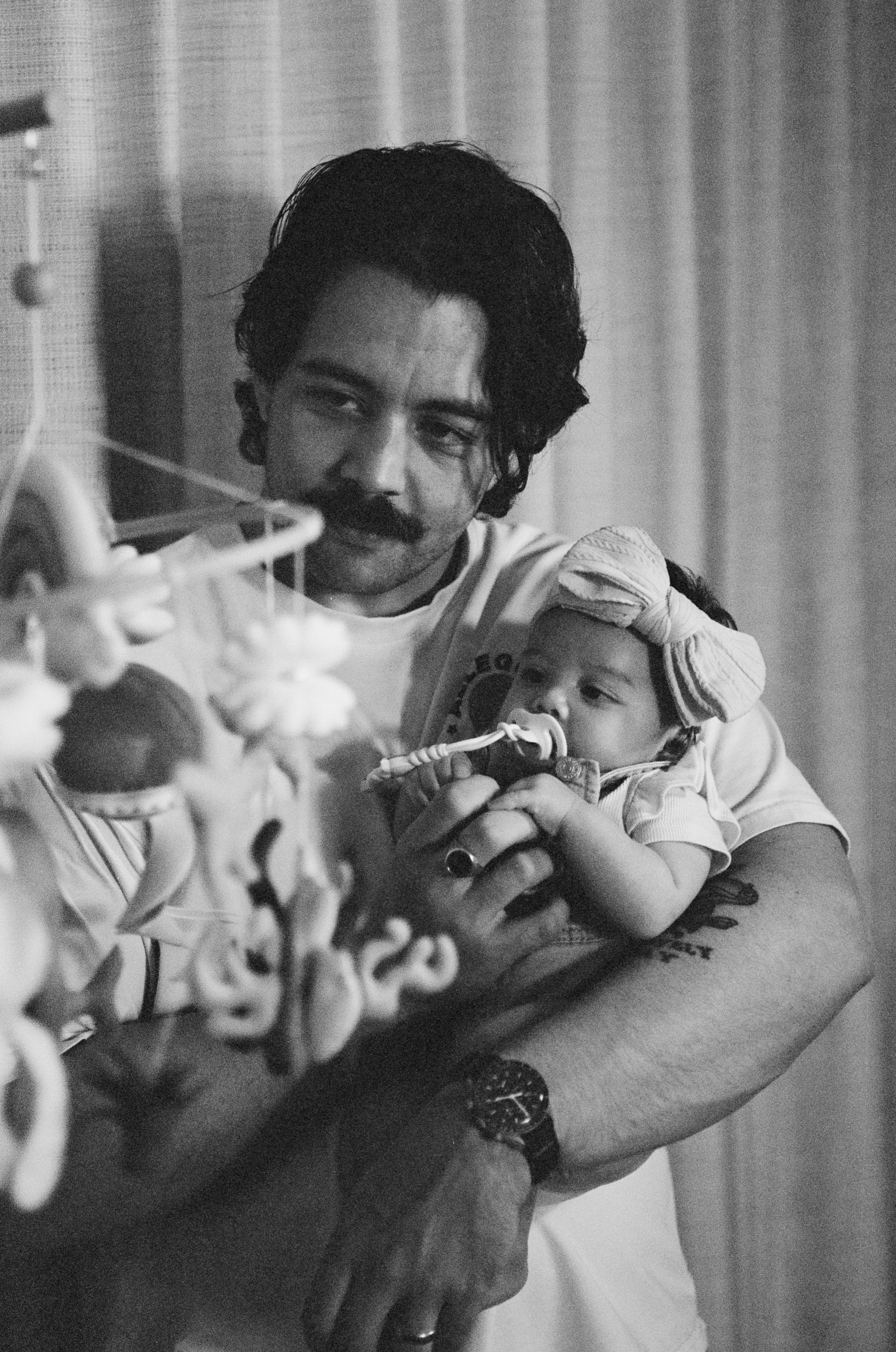 A b&w film photo of dad, showing his newborn daughter a mobile and distracting her 