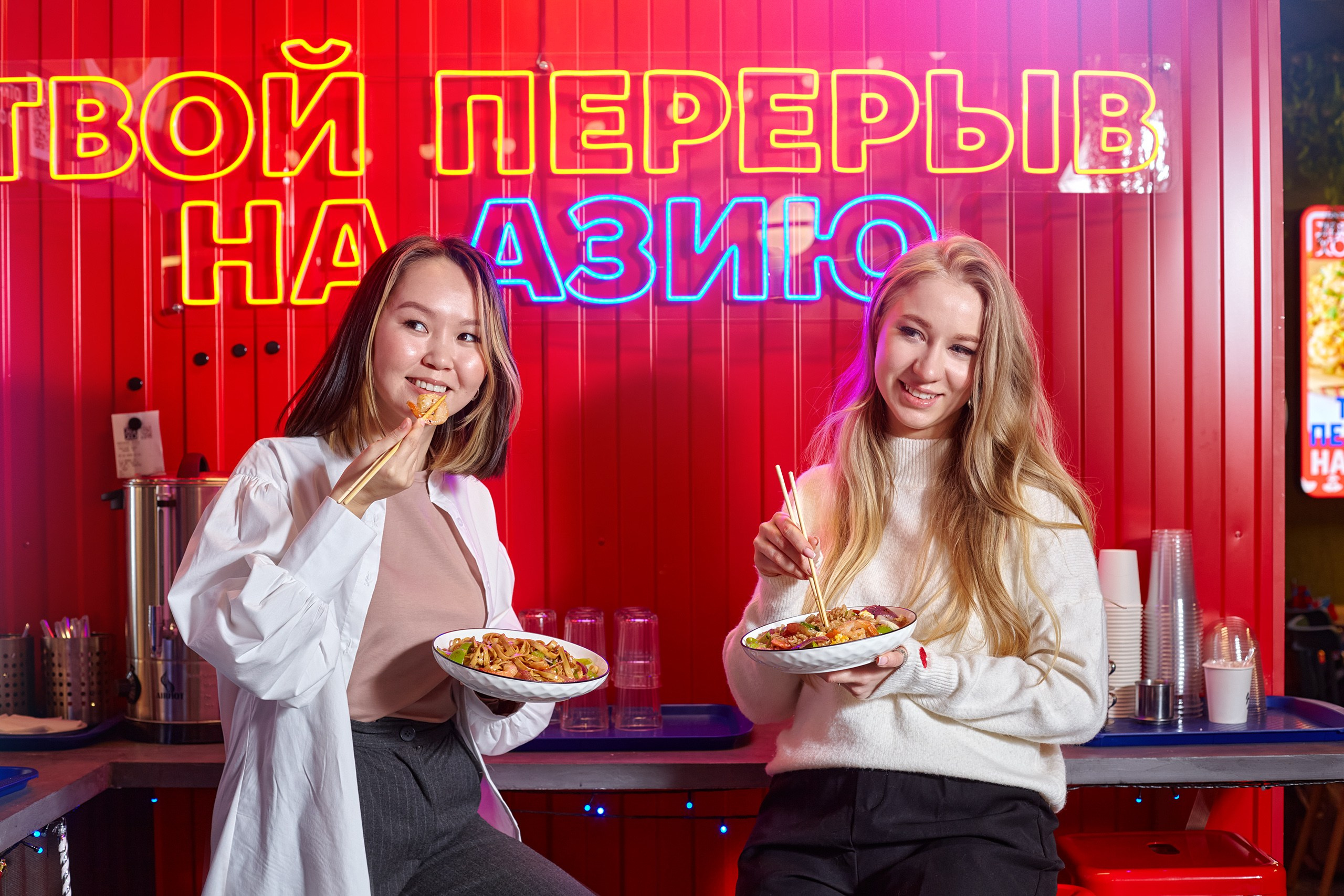 Две девушки аппетитно кушают wok палочками в интерьерах ресторана азиатской еды