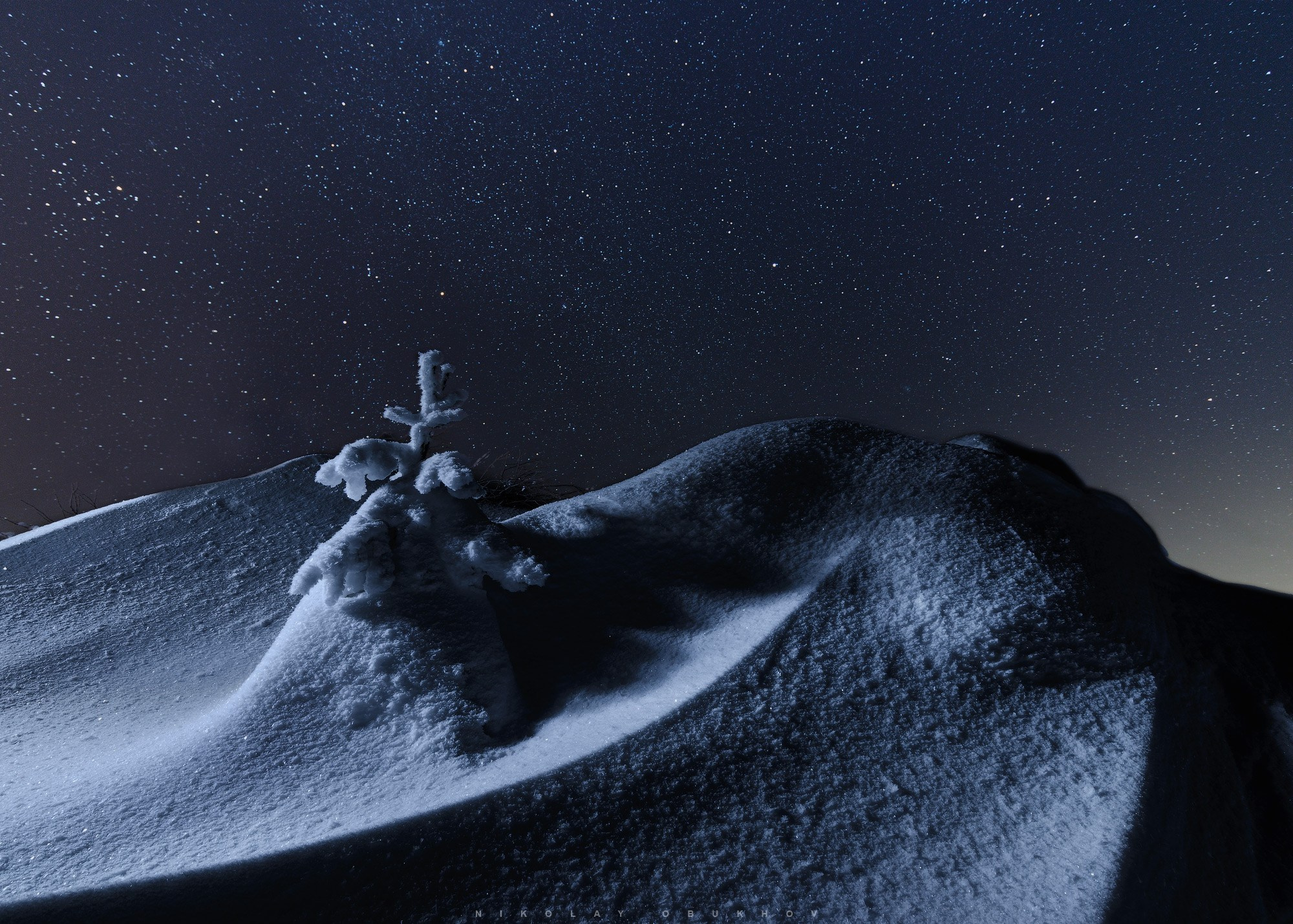 Ночной пейзаж горы Белая зимой: елочка в сугробах и звездное небо.