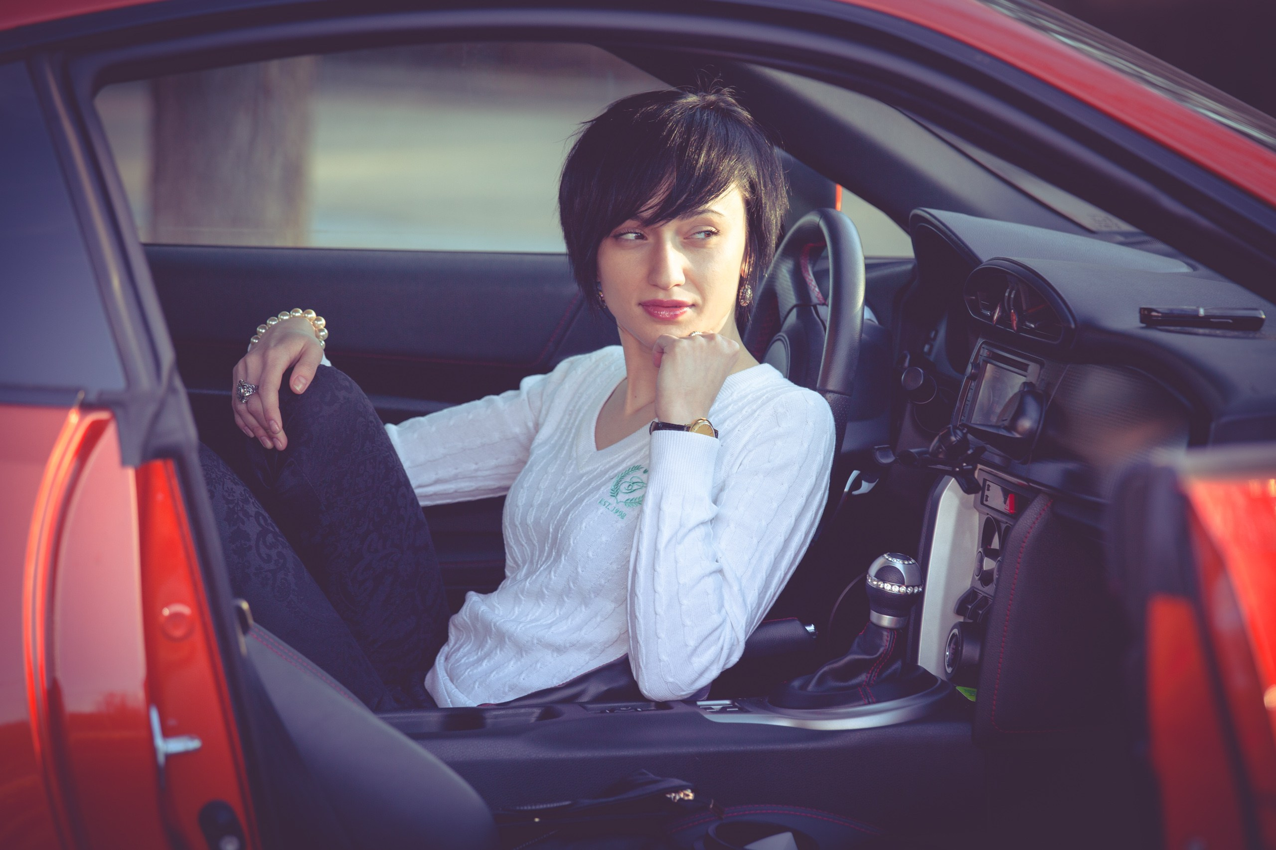 Девушка в элегантном пальто сидит за рулем современного автомобиля, сочетая классический стиль и динамичную жизнь.