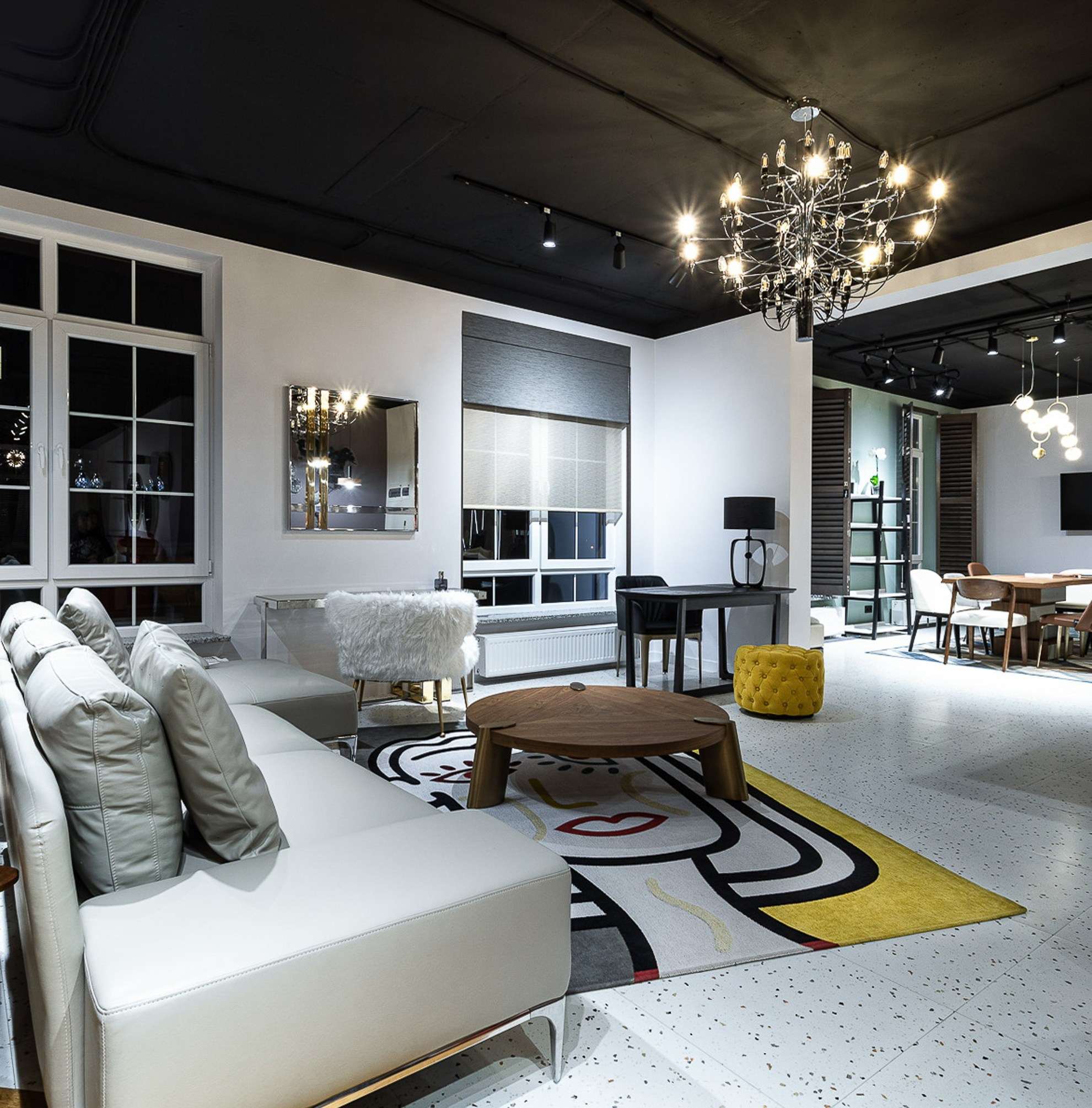 В белом зале лежит ковер, на котором стоит светлый диван.