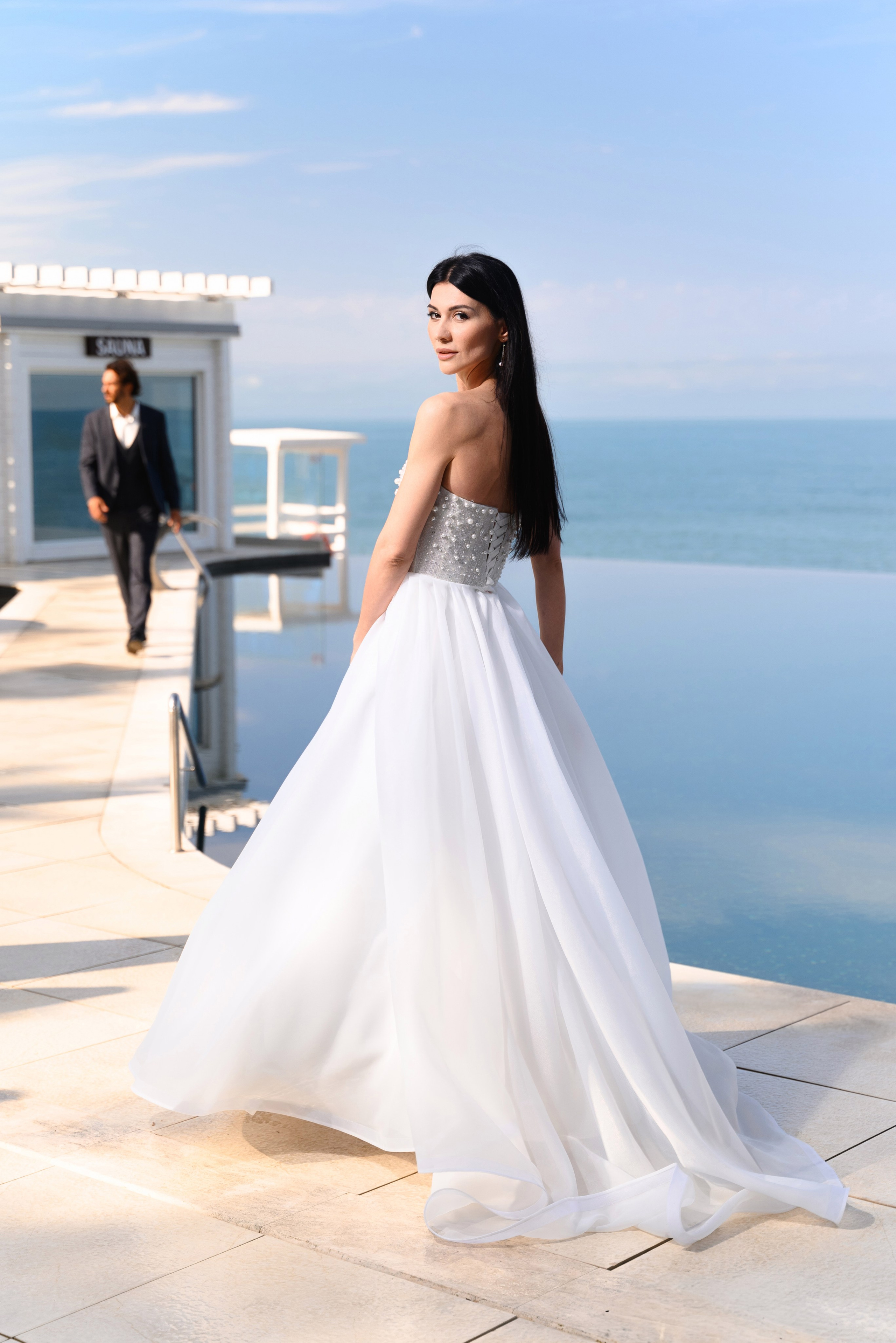 На переднем плане невеста смотрит кадр повёрнута спиной на заднем плане идёт к ней жених все это происходит на бассейне который плавно уходит в море все это происходит в городе Сочи отеле Лучезарный 