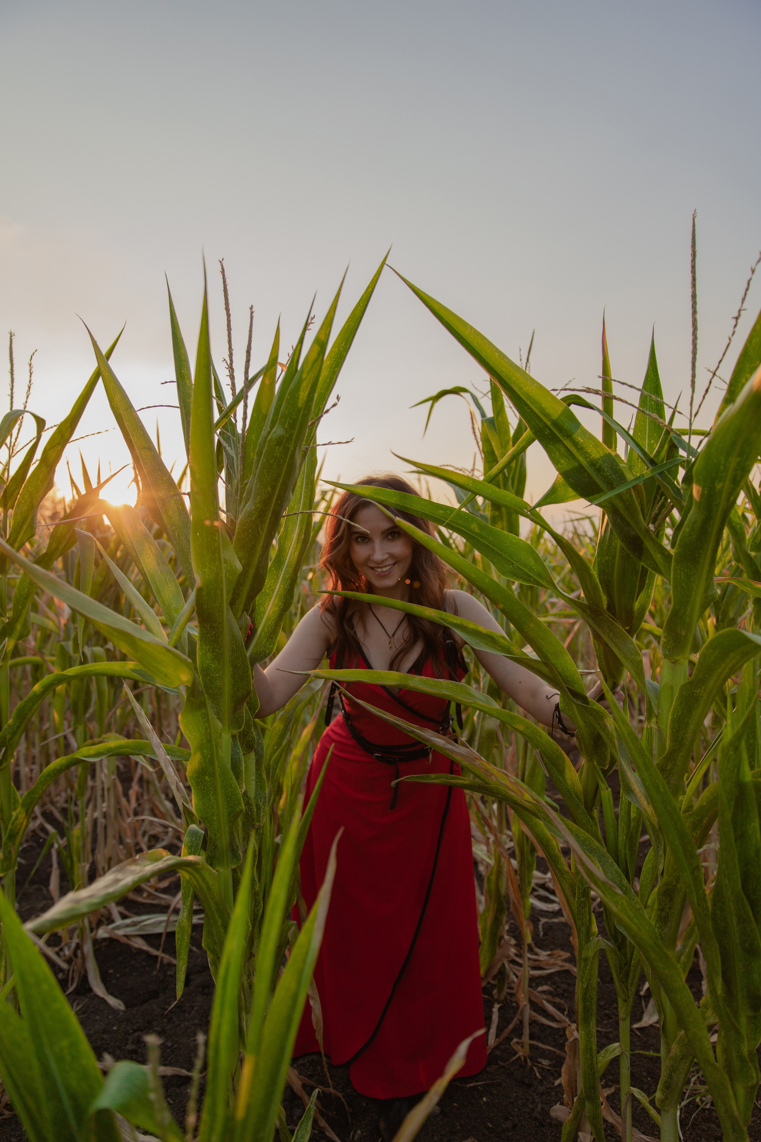 Девушка в красном платье с цветочным принтом, стоящая среди ярких подсолнухов, улыбающаяся к камере