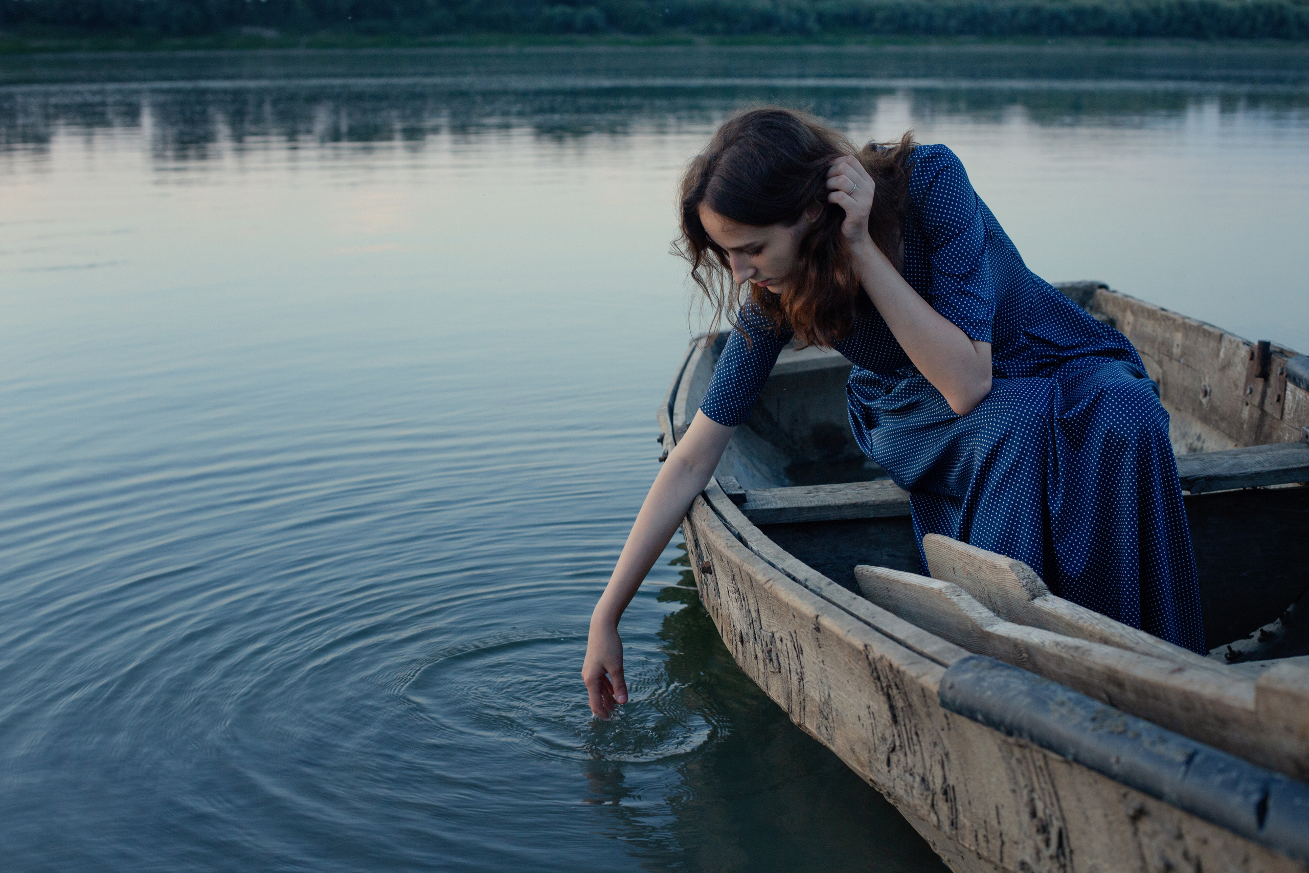 Лодка на реке, в ней сидит девушка и трогает рукой воду.