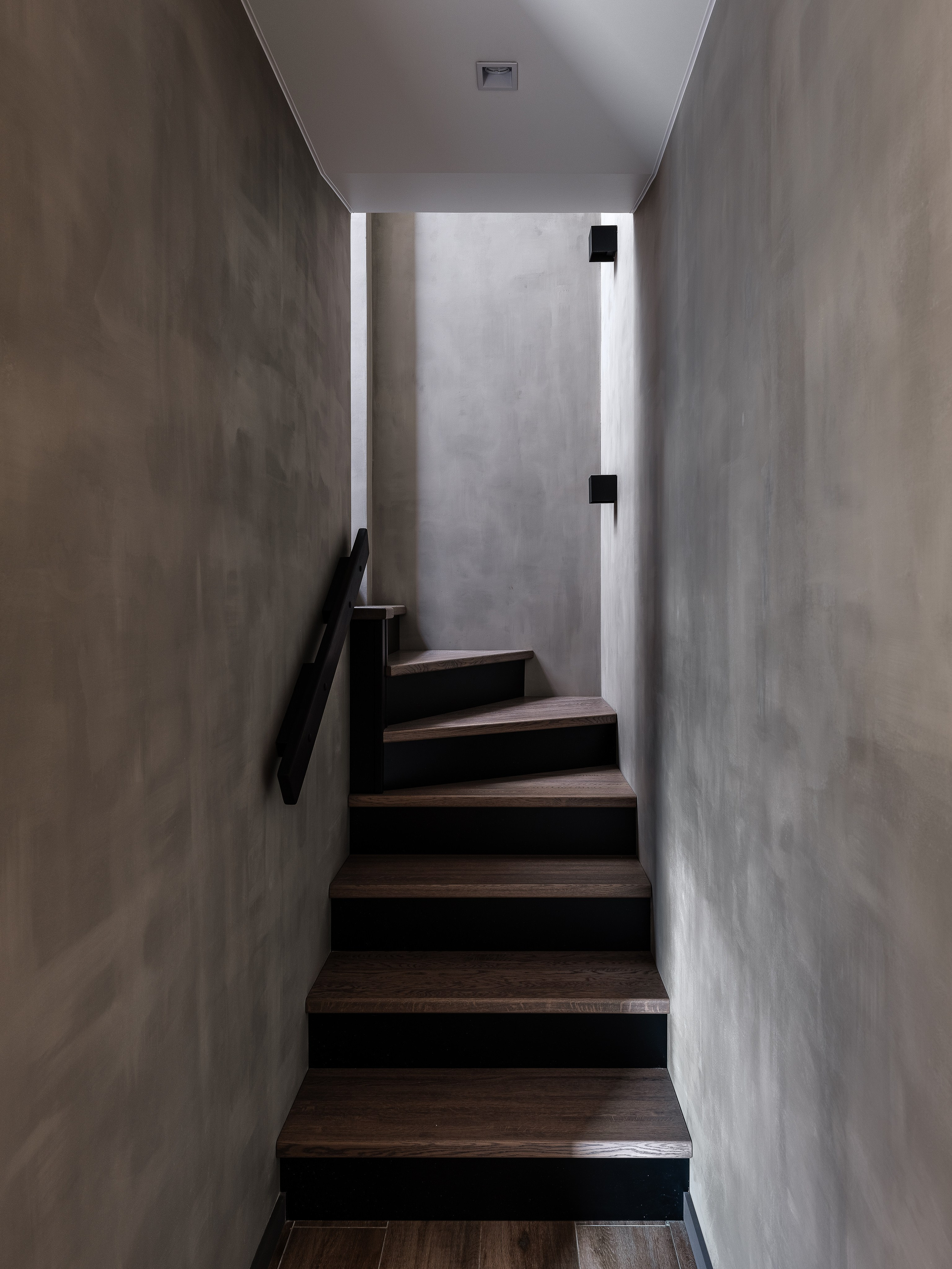 Современный лестничный холл с серыми стенами и деревянными ступенями в минимализме, чёрные акценты создают контраст. Интерьер разработан дизайнером Екатериной Мищенко, фотограф Сергей Денисенко, стильная архитектура.