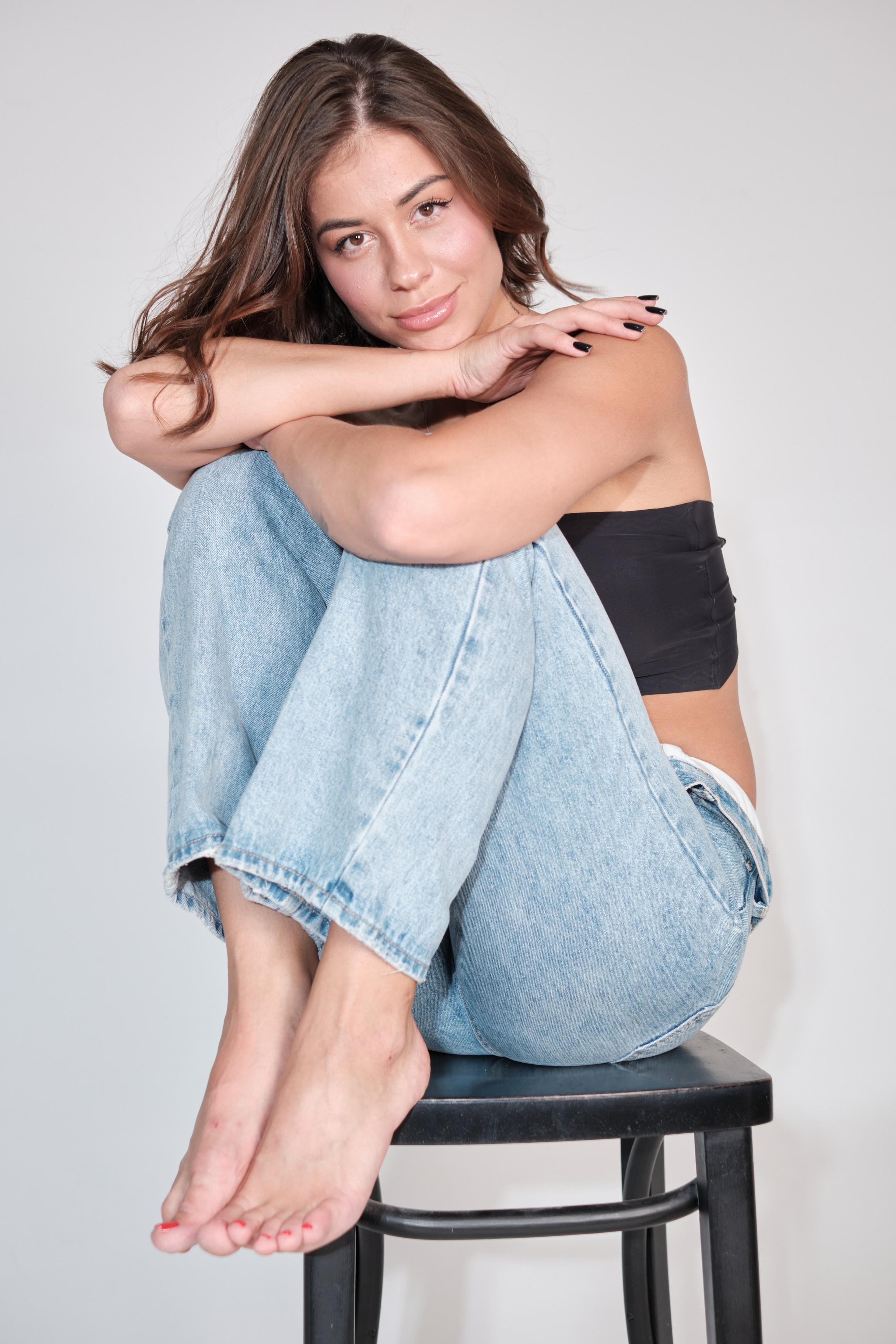 Сьемка в студии для модельного агентства, девушка в джинсах и черном топике сидит на стуле