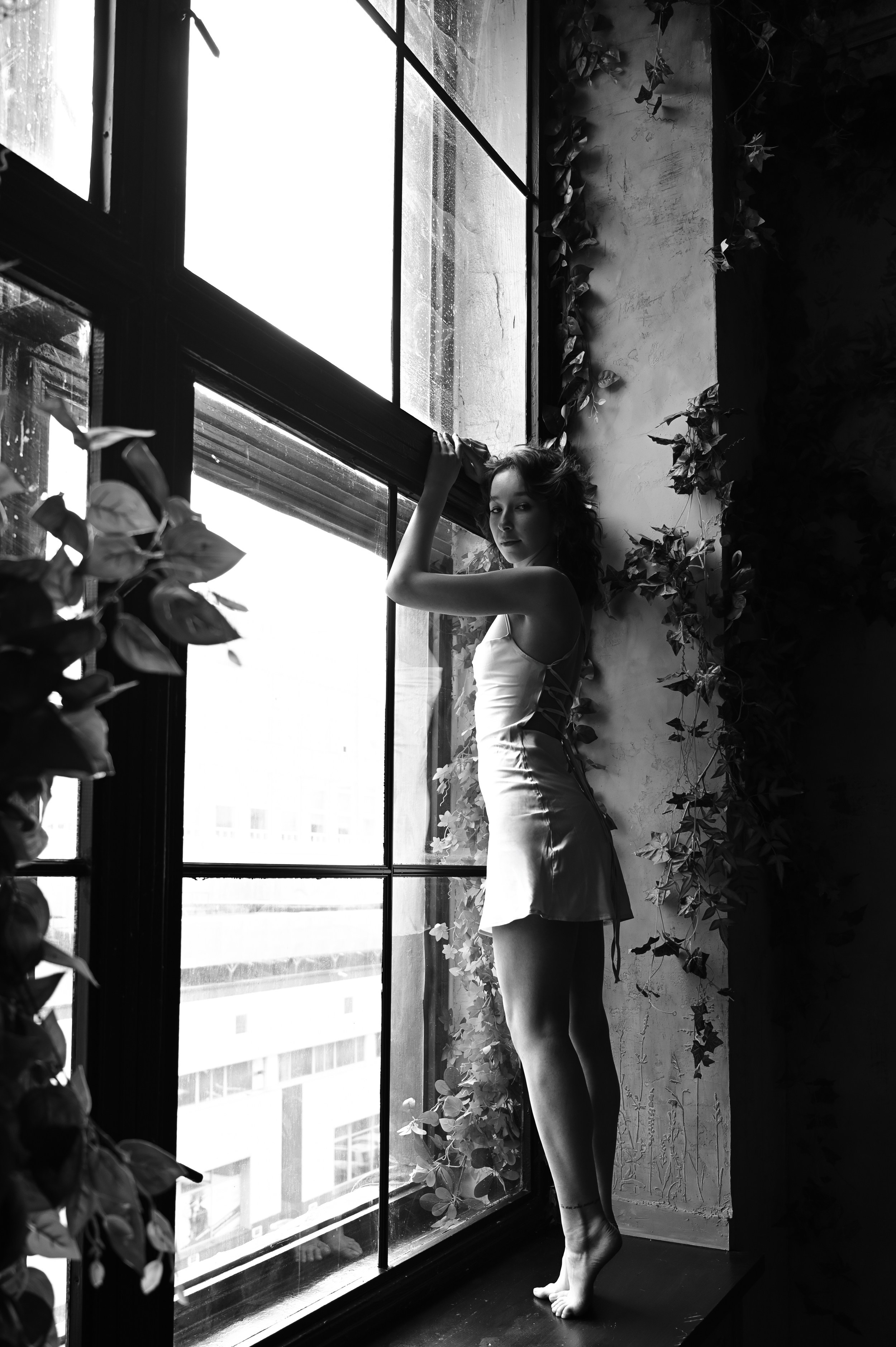 Арт-фотография девушки в студии с винтажными окнами, где живой свет подчёркивает линии тела
