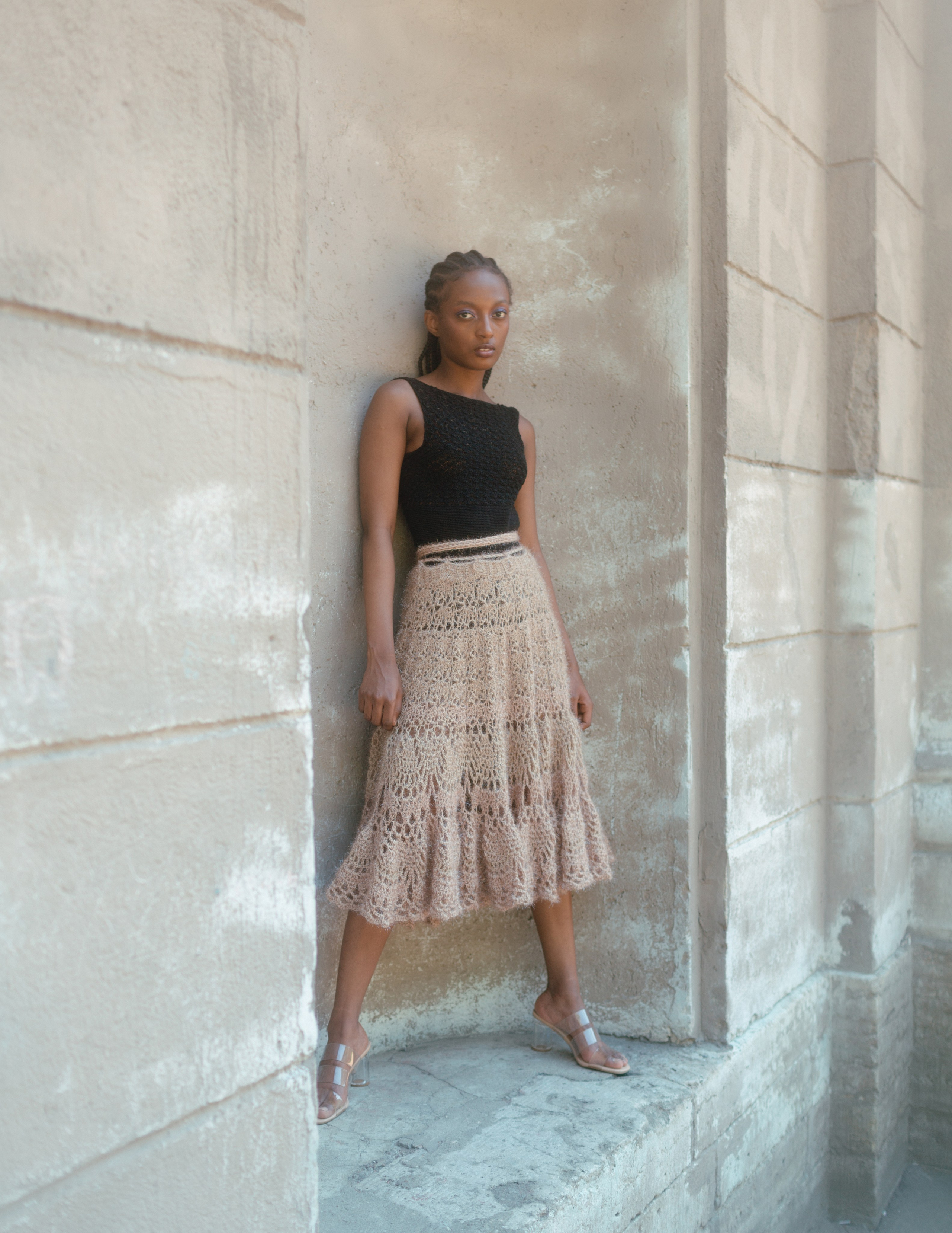 Негритянка в черном топе и розовой вязанной юбке стоит на фоне старинного здания.