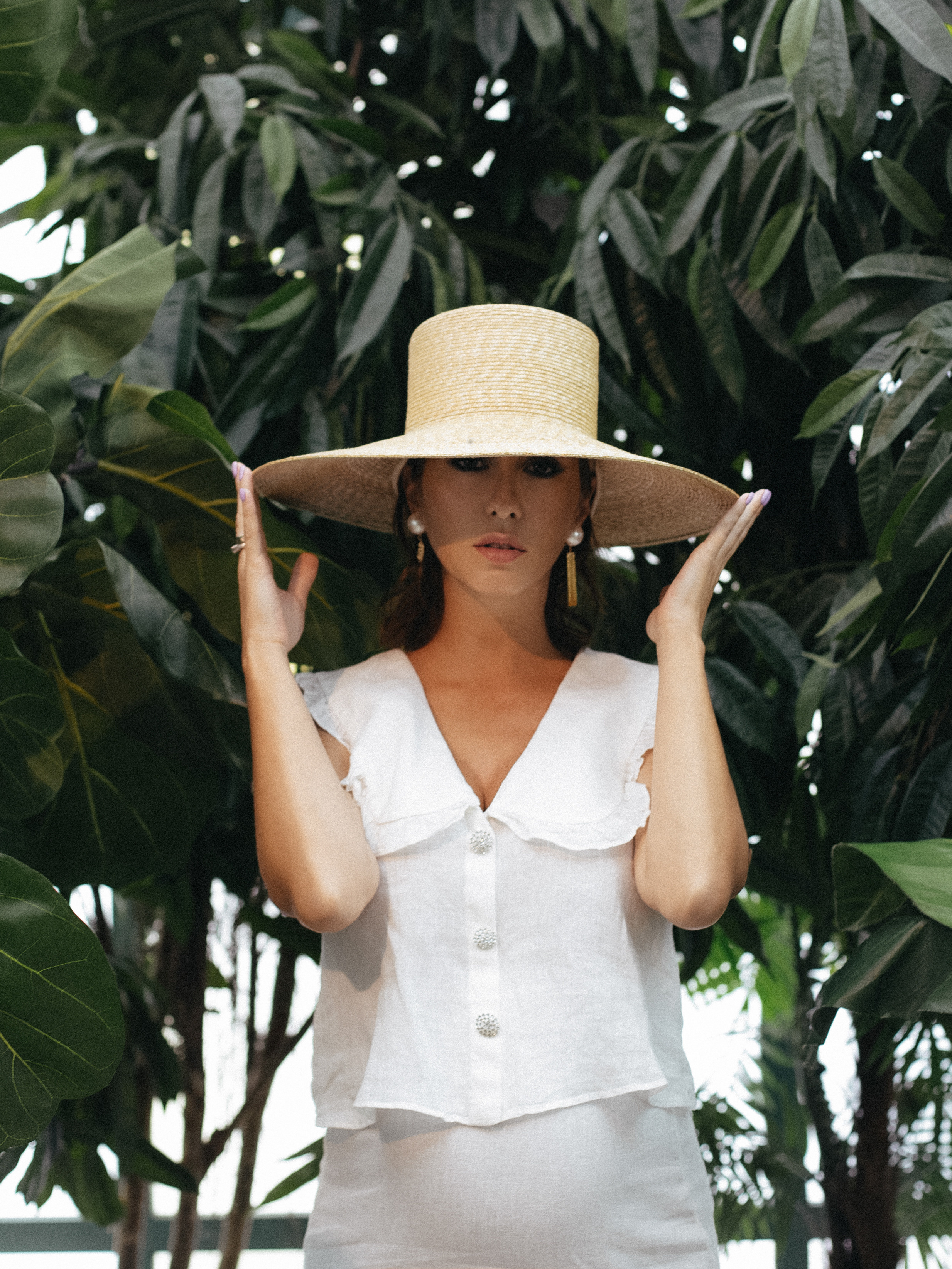 Беременная девушка в белом платье и в соломенной шляпе среди тропических пальм и деревьев