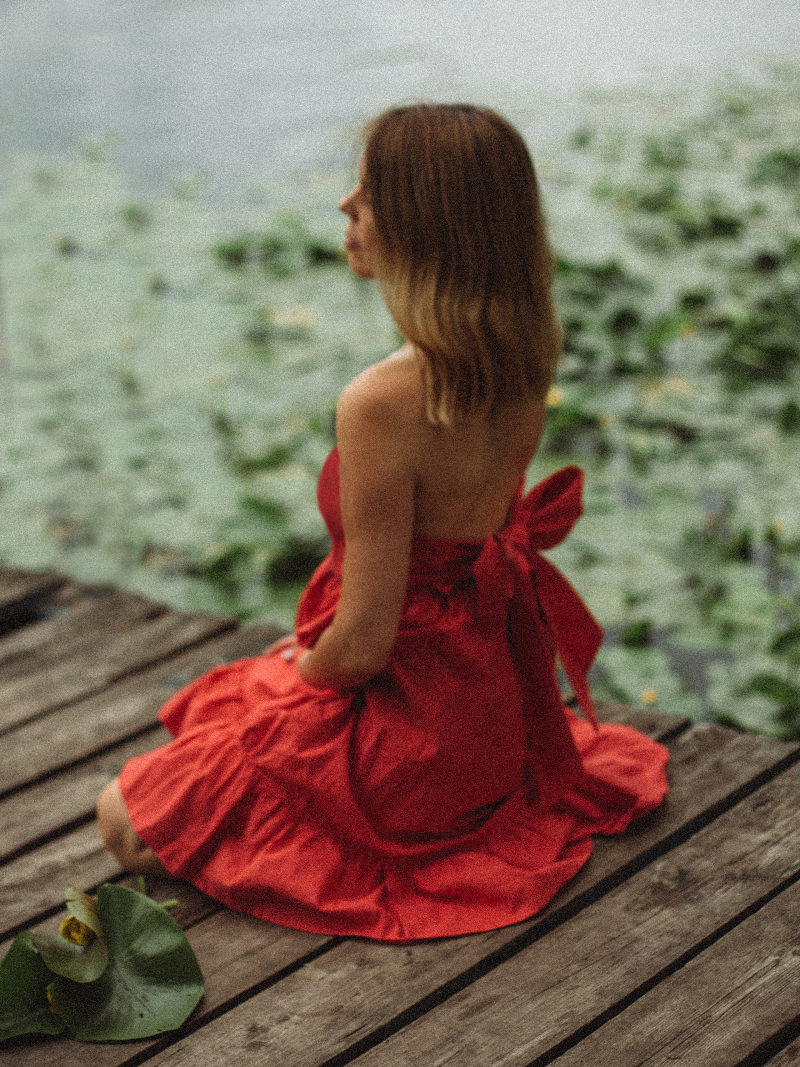 беременная девушка сидящая на пирсе в красном платье среди кувшинок