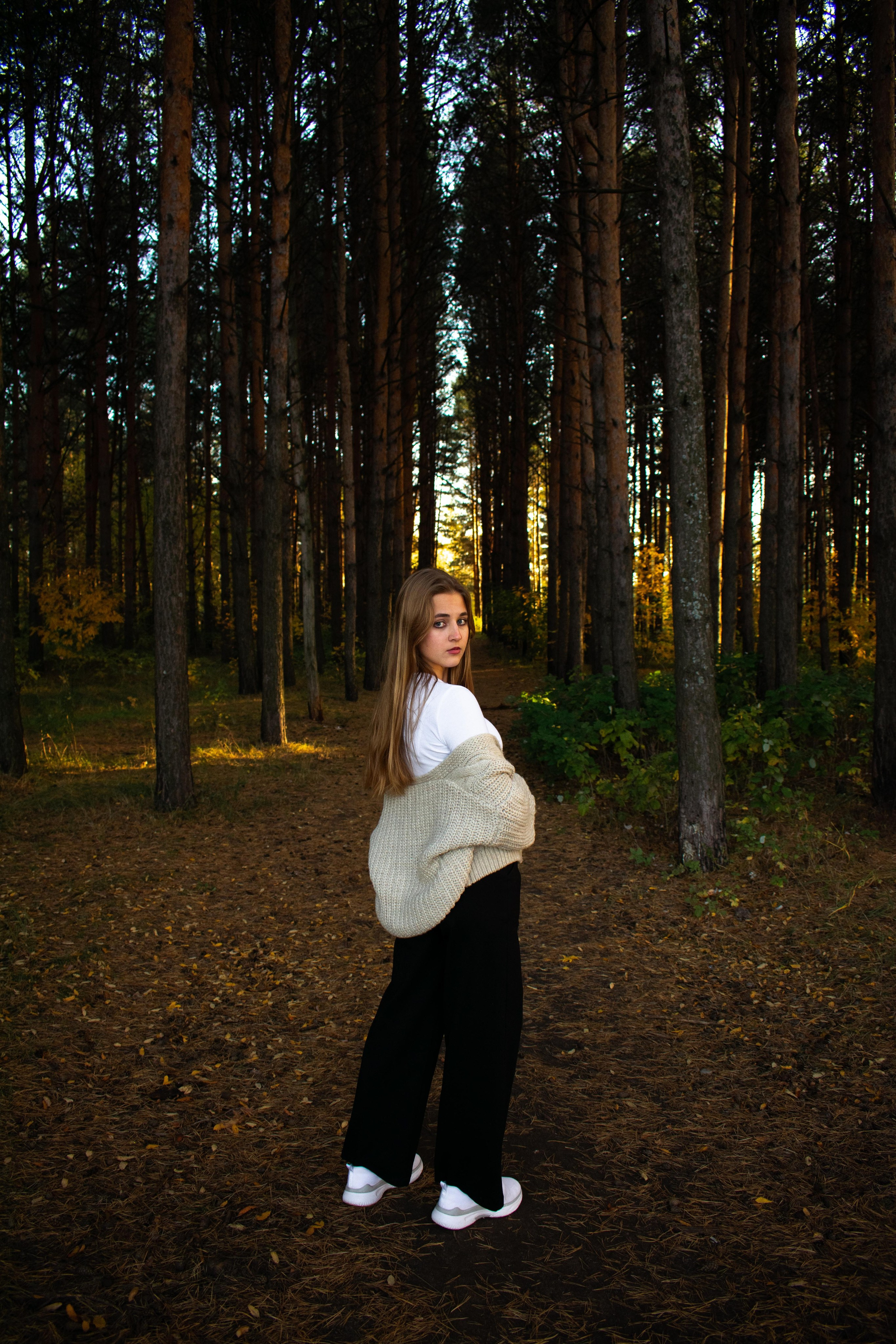 Девушка позирует в сосновом лесу в белой футболке и серой кофте