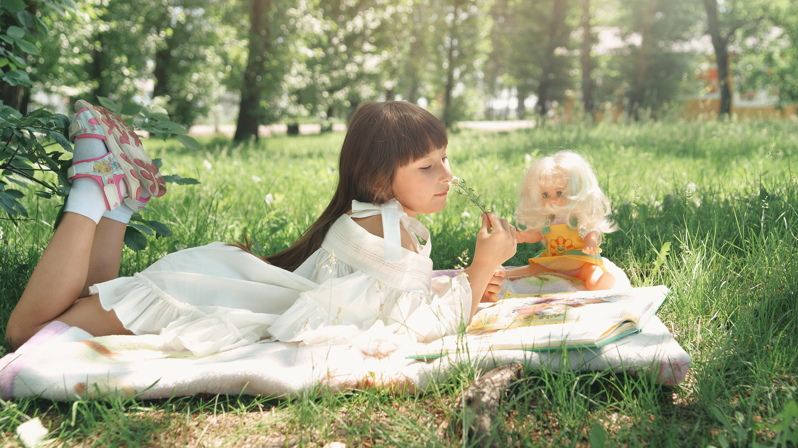 Детская фотосессия летом - девочка на траве читает книгу с куклой