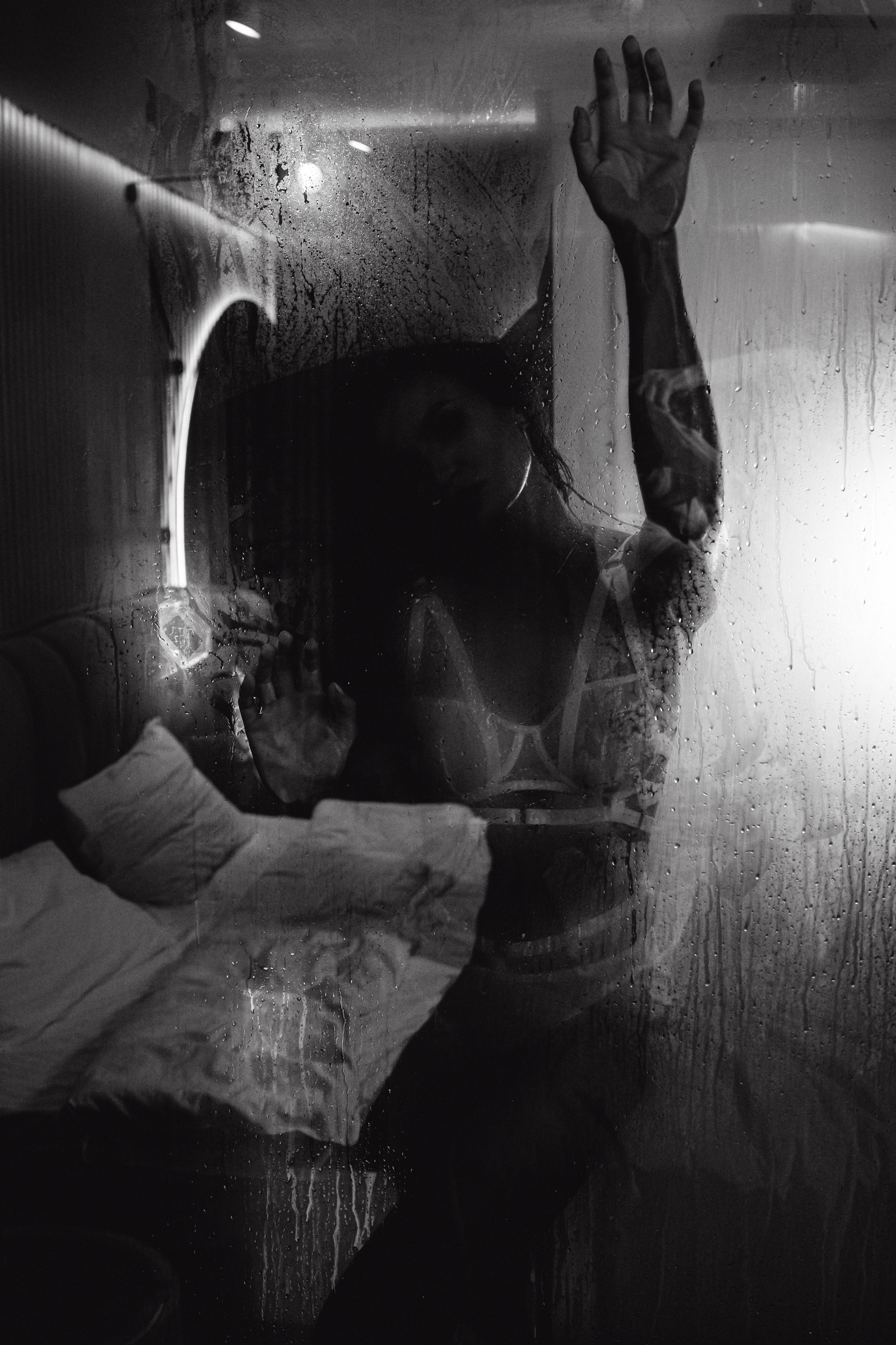 "Сквозь стекло с каплями воды проступает божественная красота девушки, создавая эффект загадочности и притягательности."