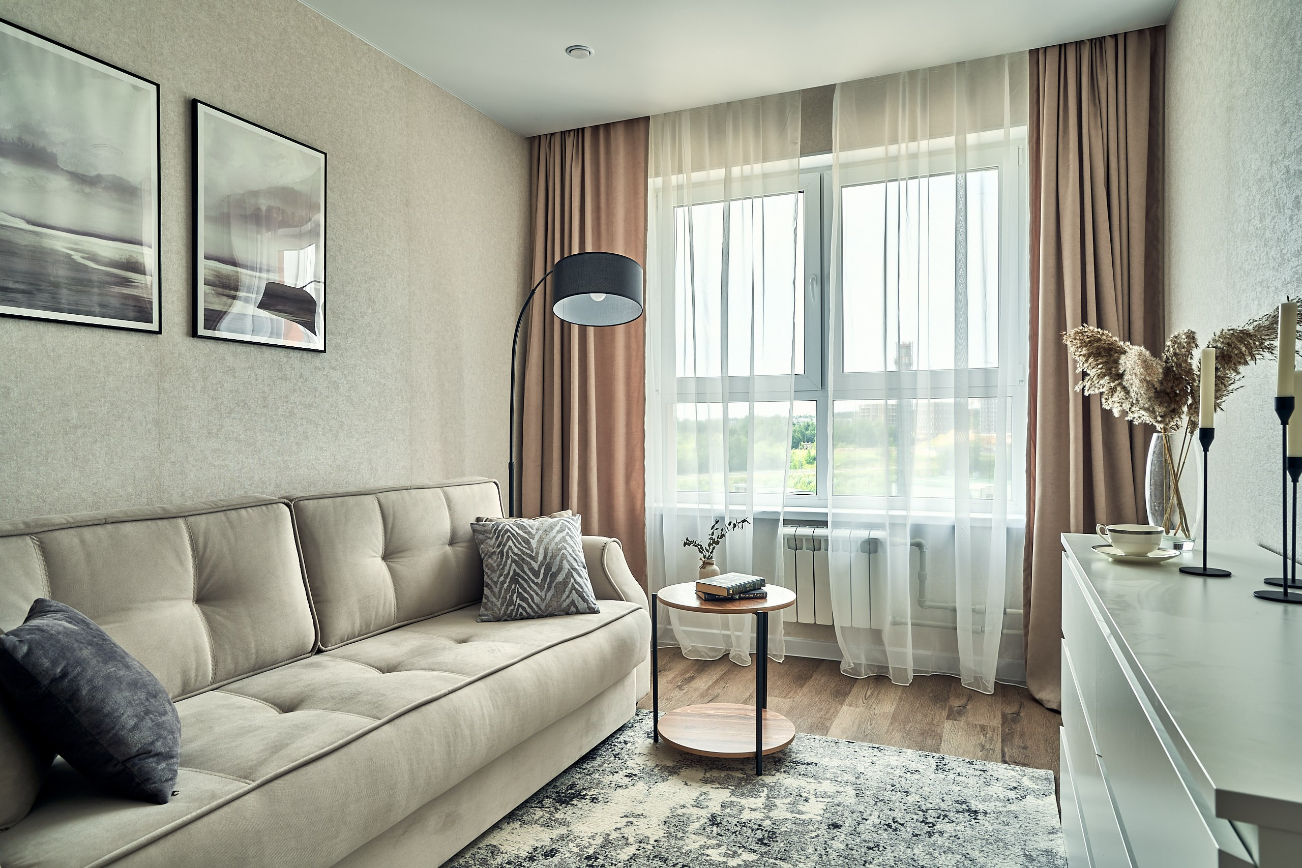 Интерьерная съемка комнаты в подмосковных апартаментах с диваном, букетом, большим окном и интерьерной живописью на стене