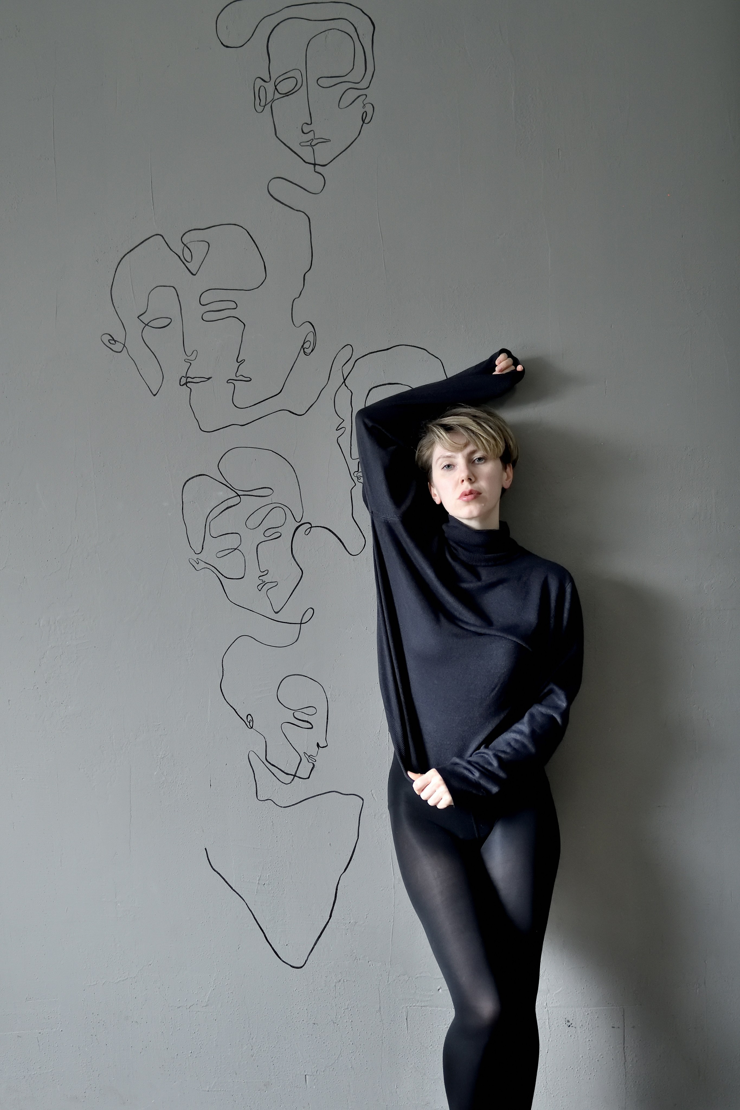 Красивая, чувственная фотосессия девушки в сером свитере у серой стены.