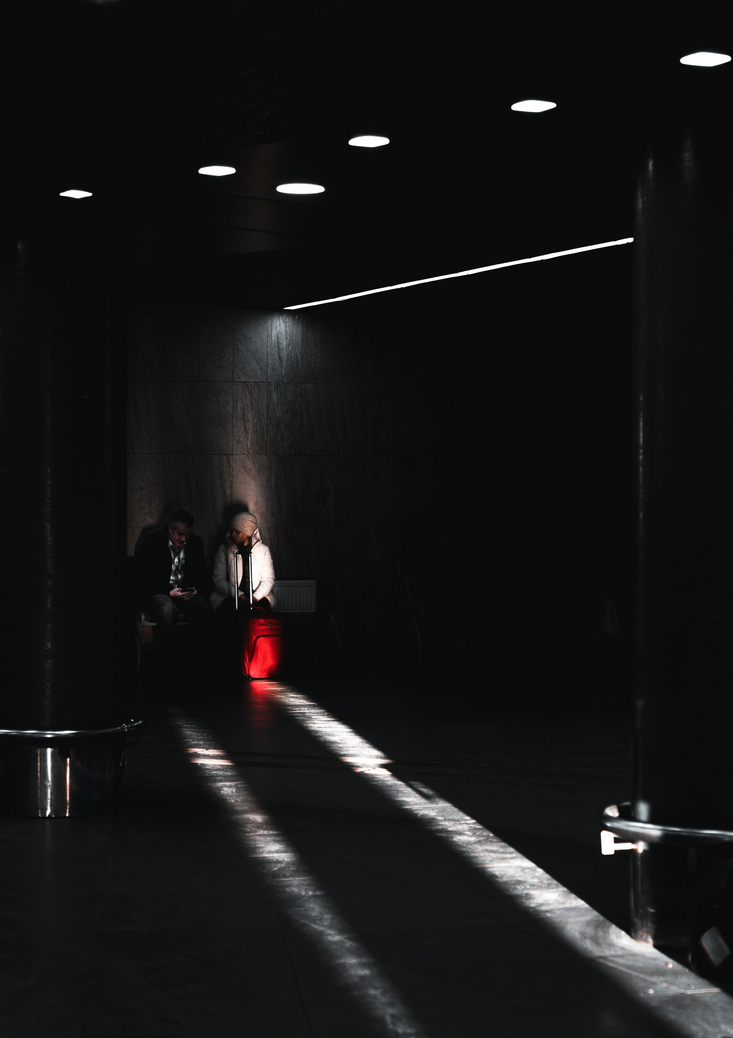 Ладожский вокзал. Пара с чемоданом ждёт в тёмном современном вестибюле вокзала, силуэты на фоне неонового света, городской Санкт-Петербург, street mood, фотограф Евгений Мальцев.