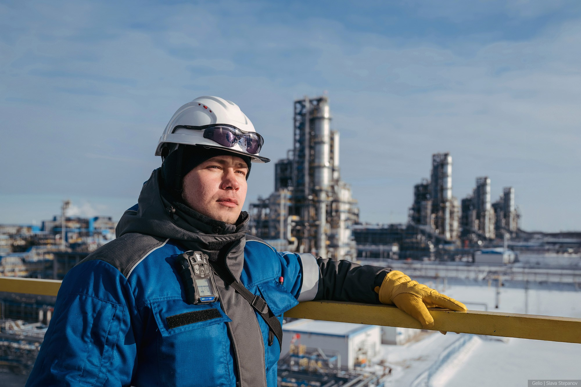 Работник газового промысла в спецодежде смотрит вдаль на фоне индустриального пейзажа