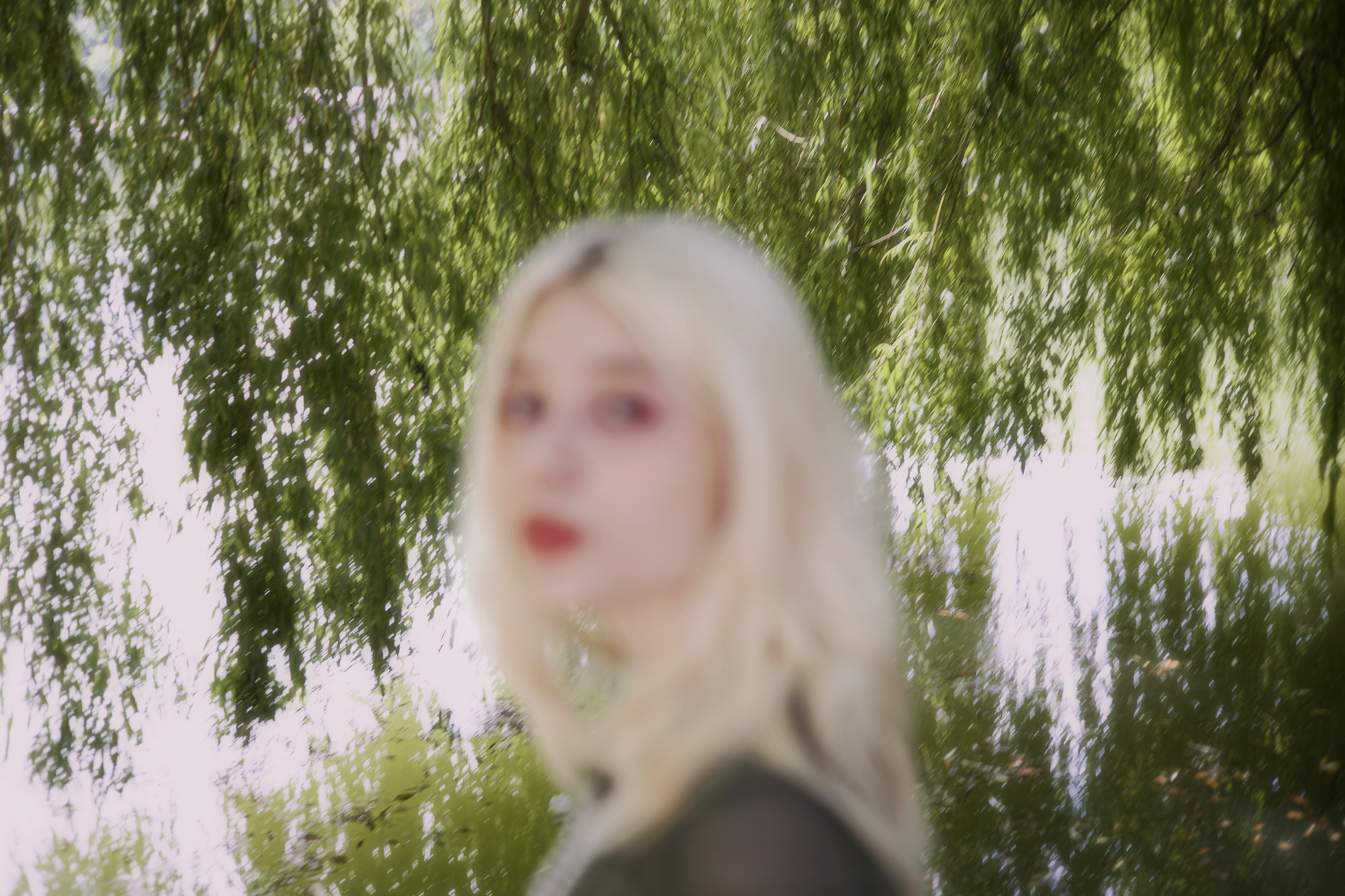 Девушка позирует под деревом на берегу пруда в летнем парке