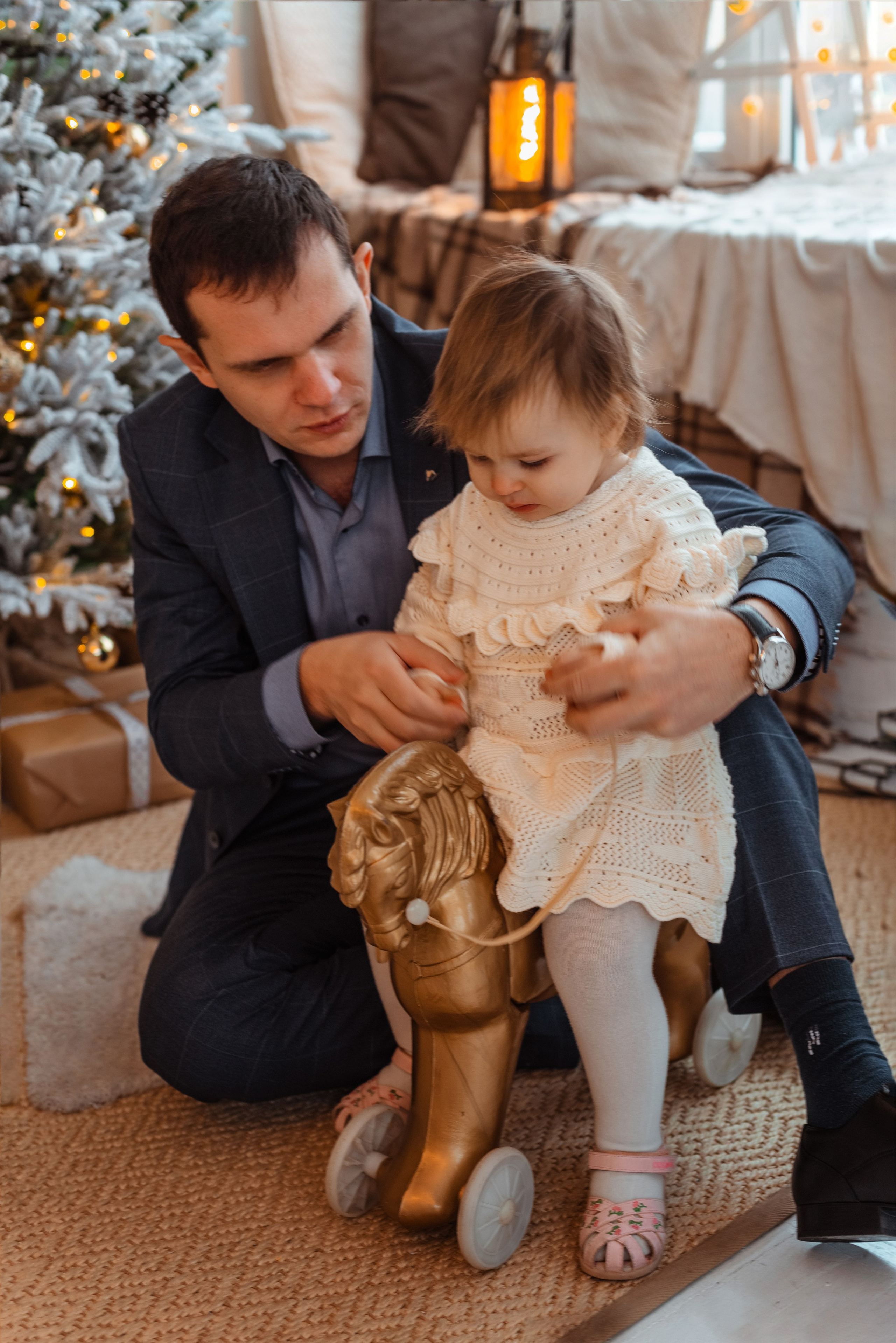 Семейная фотосессия на Новый Год: папа и дочка играют на фоне украшенной елки.