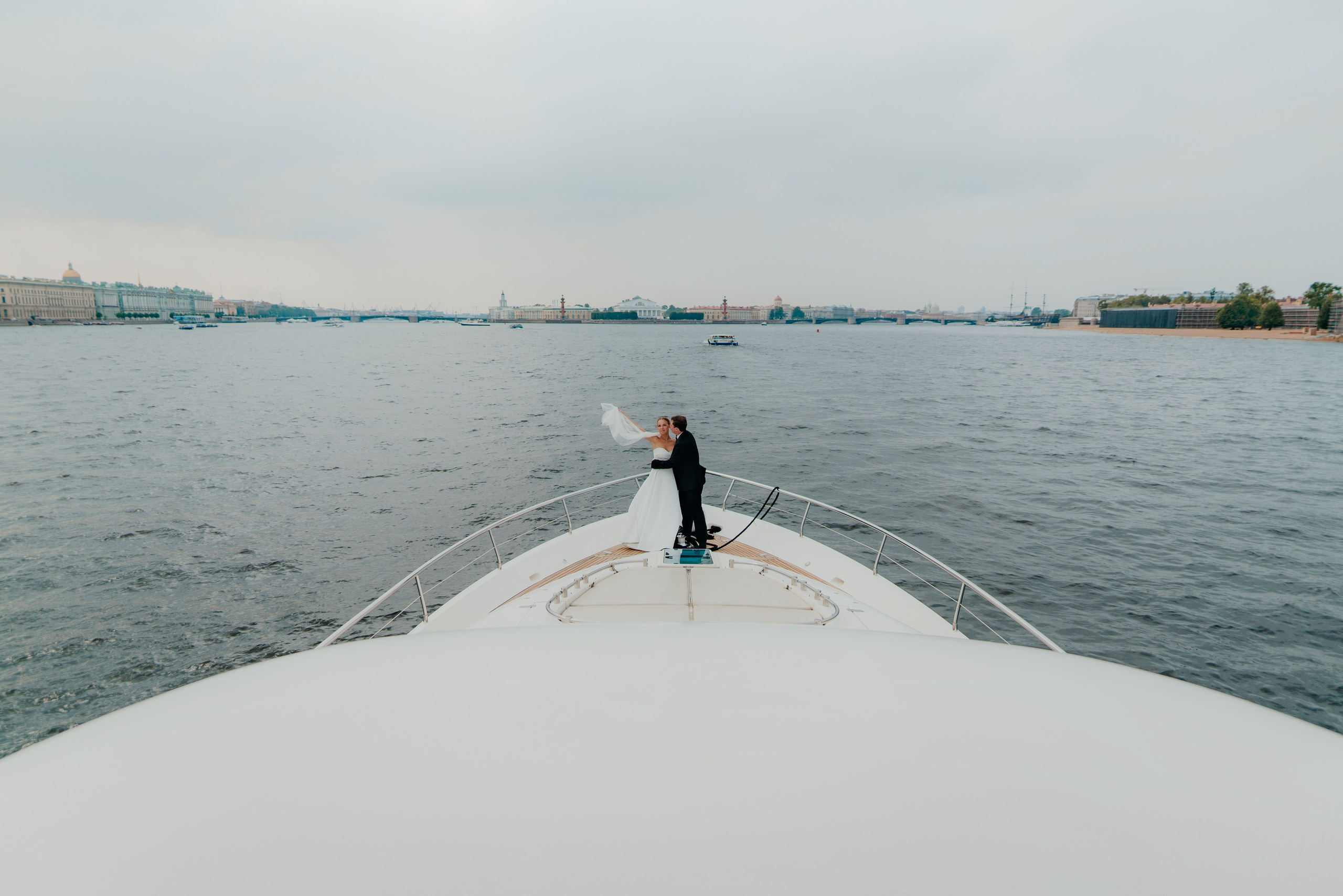 невеста и жених обнимают друг друга на носу большой яхты в акватории Невы