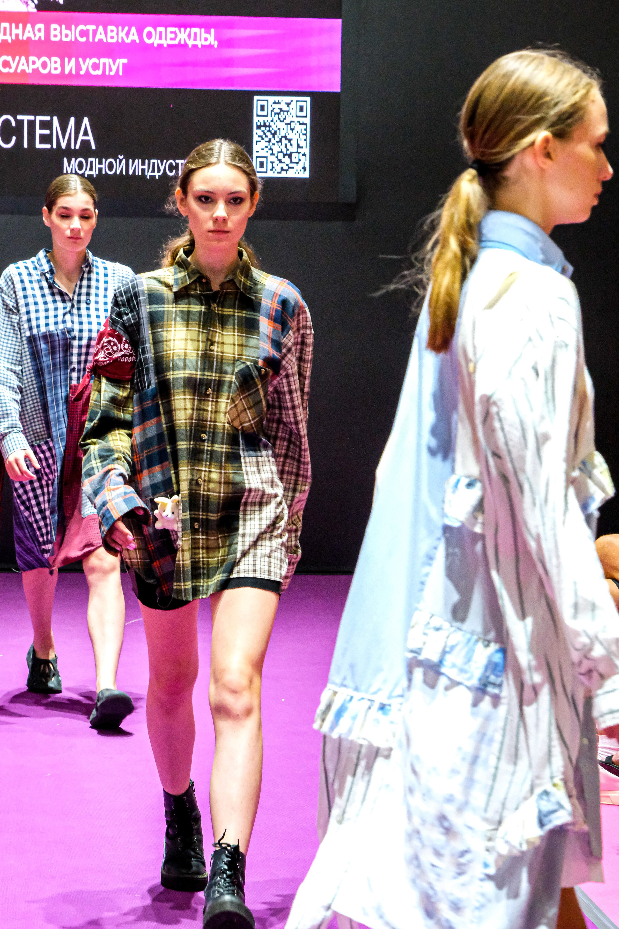  "Модели в ярких нарядах проходят по подиуму во время показа мод, освещенные яркими софитами и окруженные восторженными зрителями."